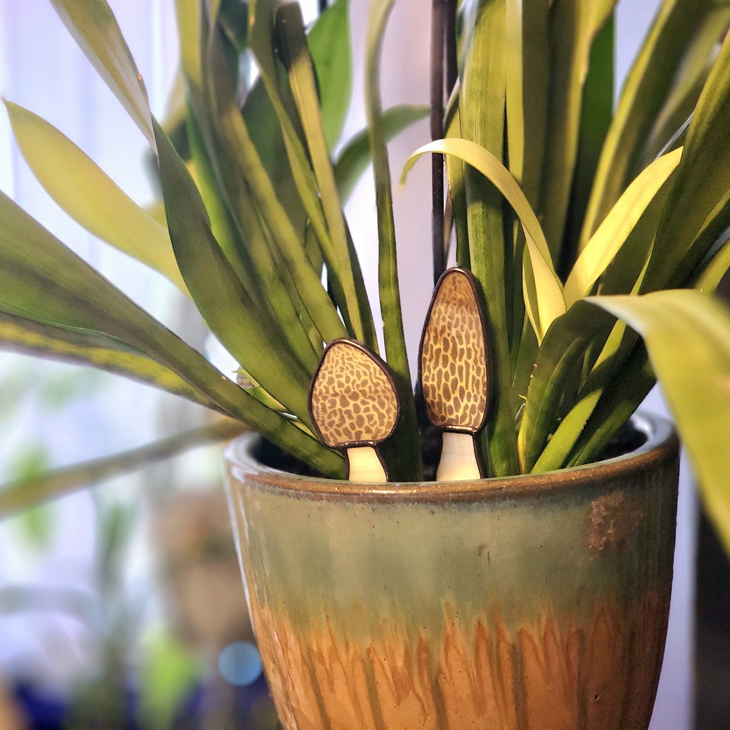 Pair of stained glass morel mushroom plant stakes in a decorative potted planter on a blurred background