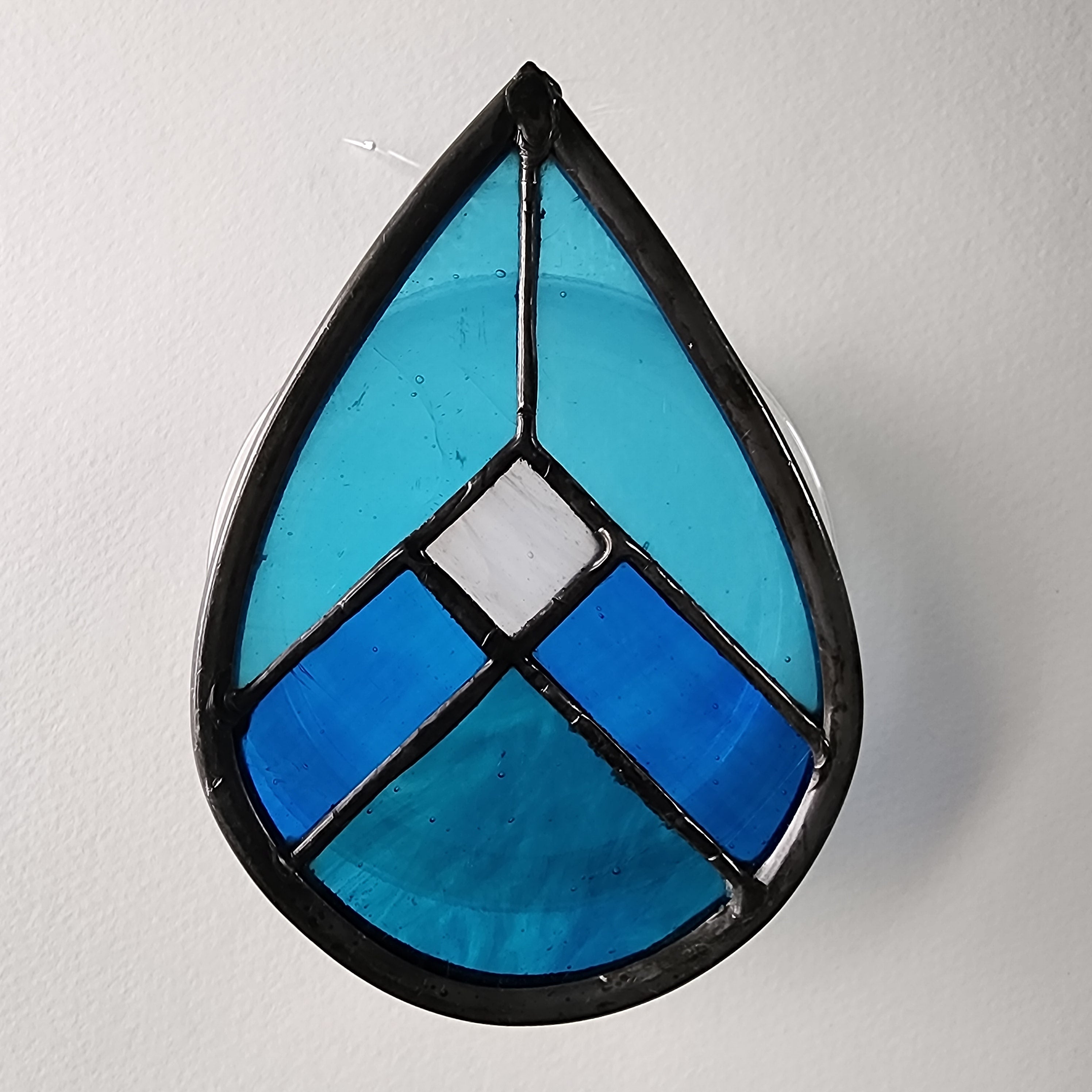 Teardrop-shaped stained glass piece with blue and black design on a white background
