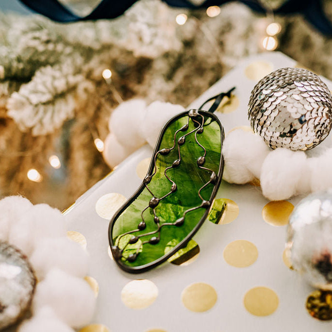 Decorative Christmas Pickle ornament  on a white gift with gold polka dots, surrounded by festive decorations.