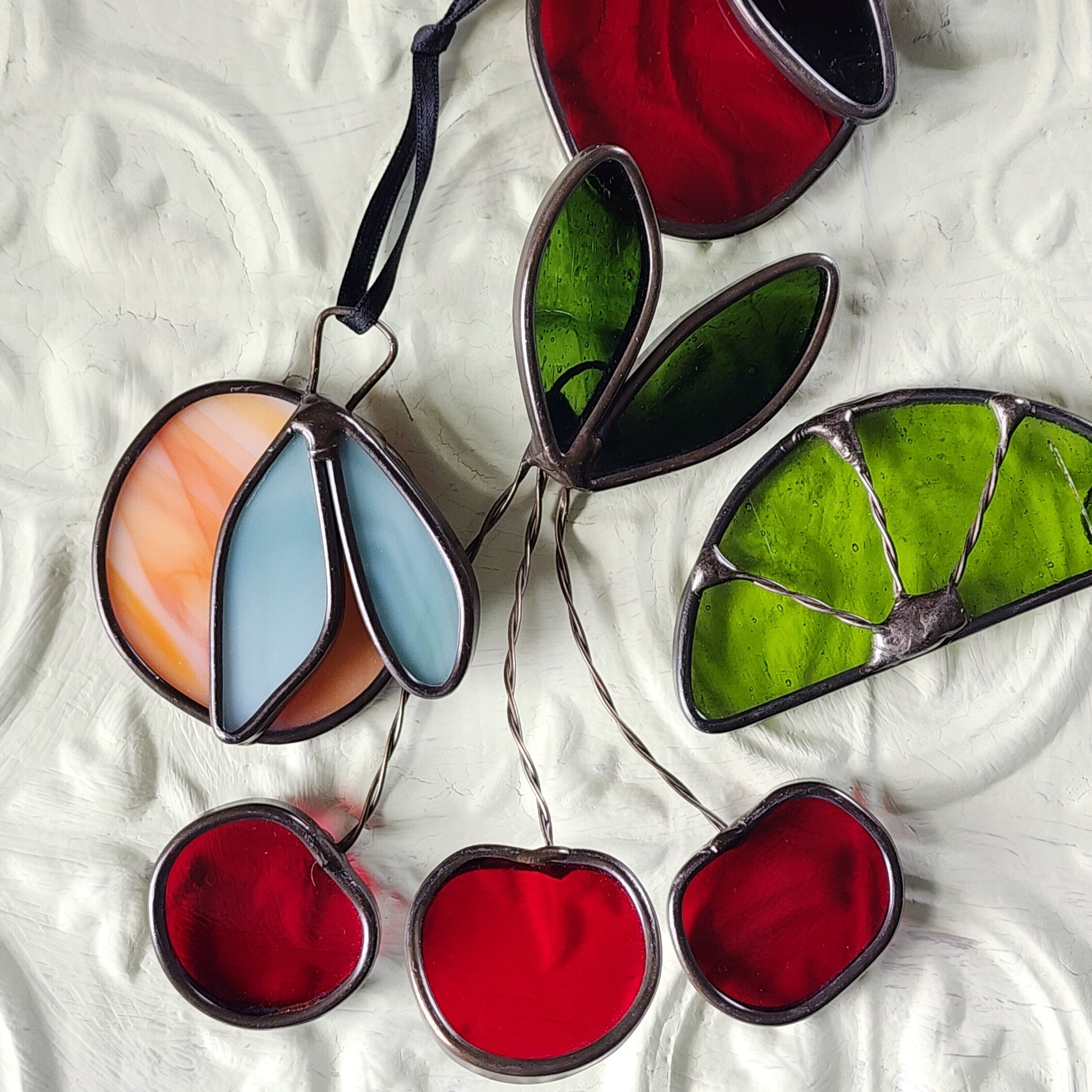 Colorful stained glass fruit suncatchers on a textured white background