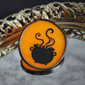 Black silhouette of a cauldron with steam on an orange stained glass, displayed on a decorative background