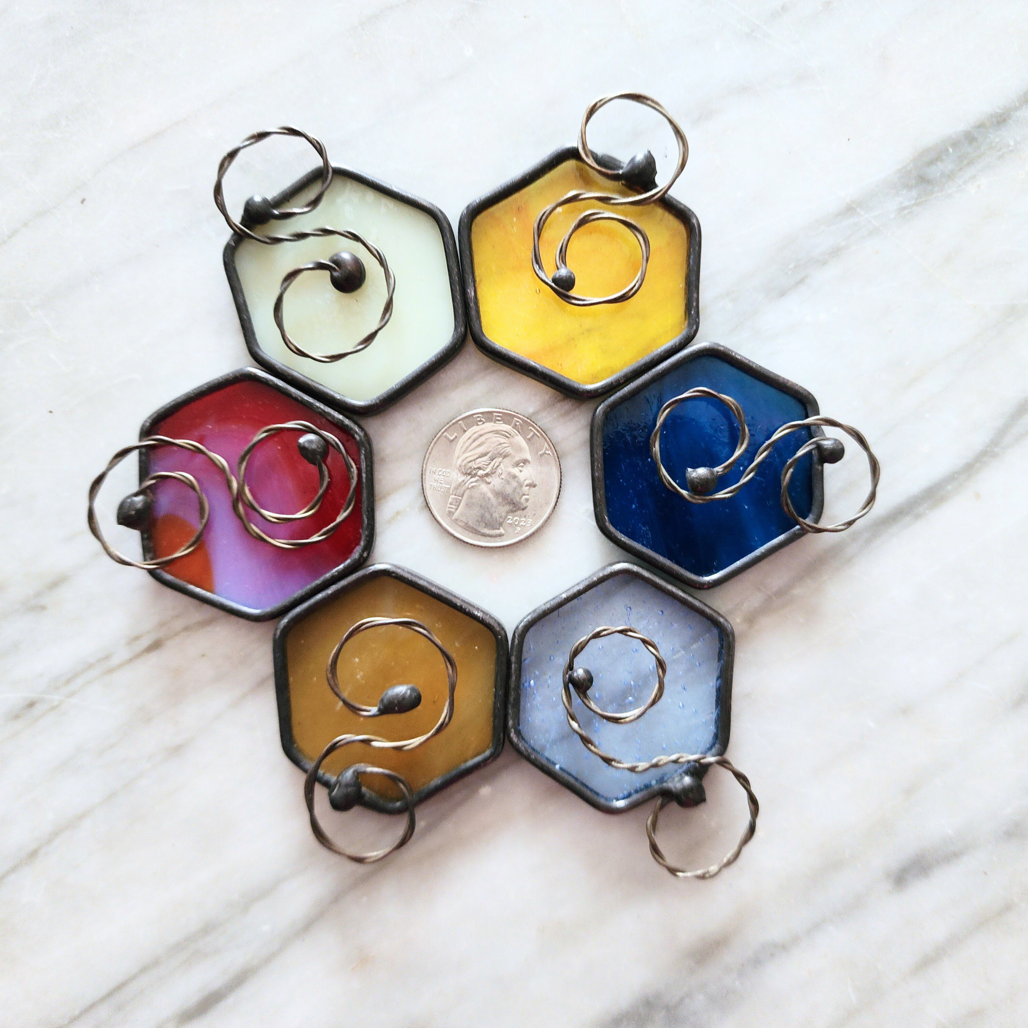 Hexagonal stained glass charms in various colors arranged around a coin on a marble surface.