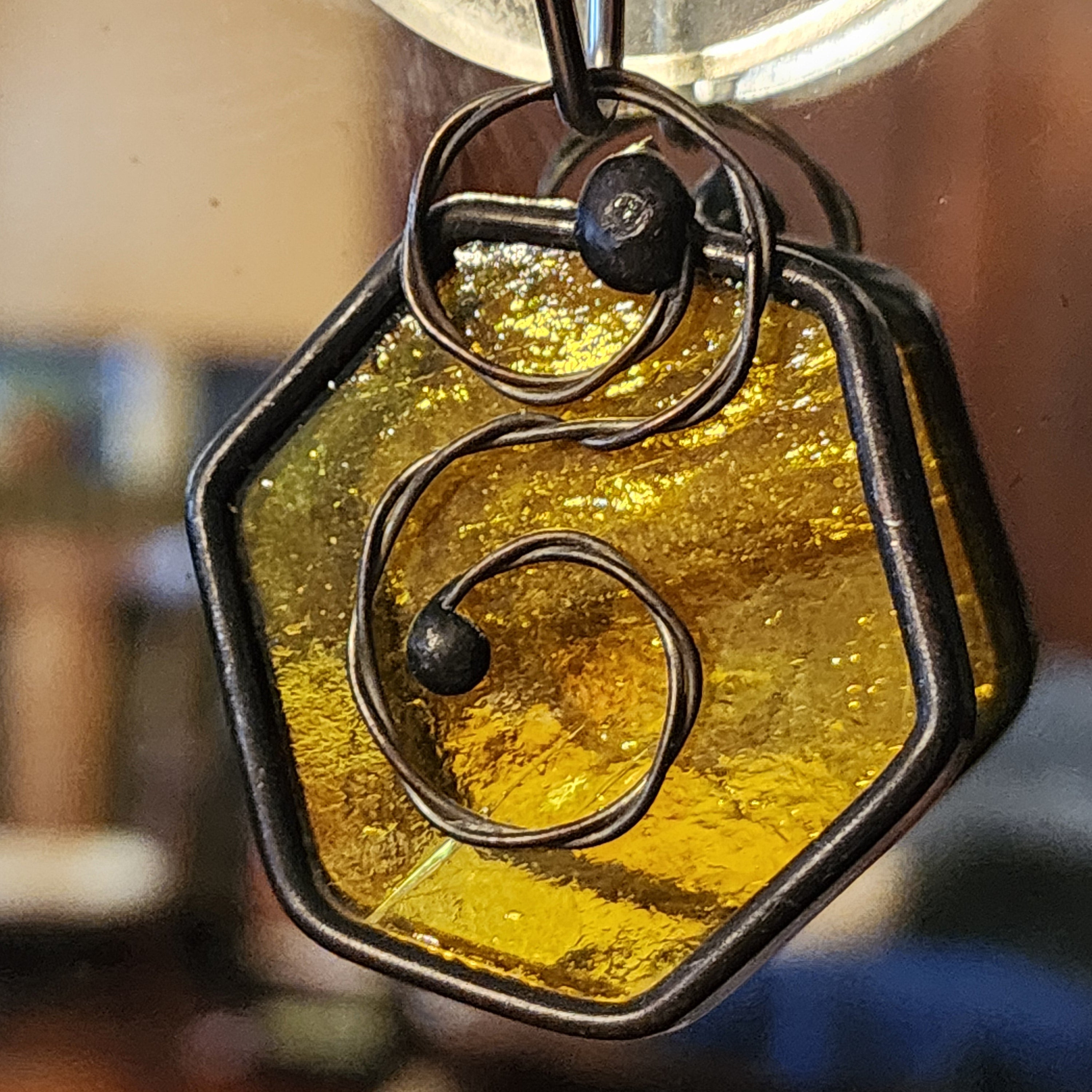 Amber yellow mini hexagon stained glass suncatcher car charm, blurred indoor background