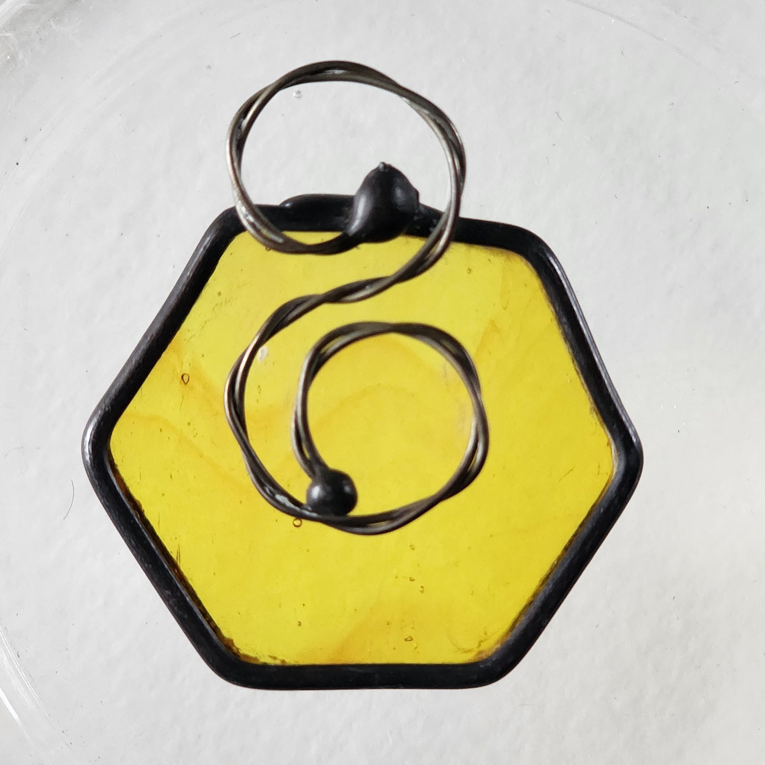 Yellow hexagonal suncatcher charm with black border on a clear background