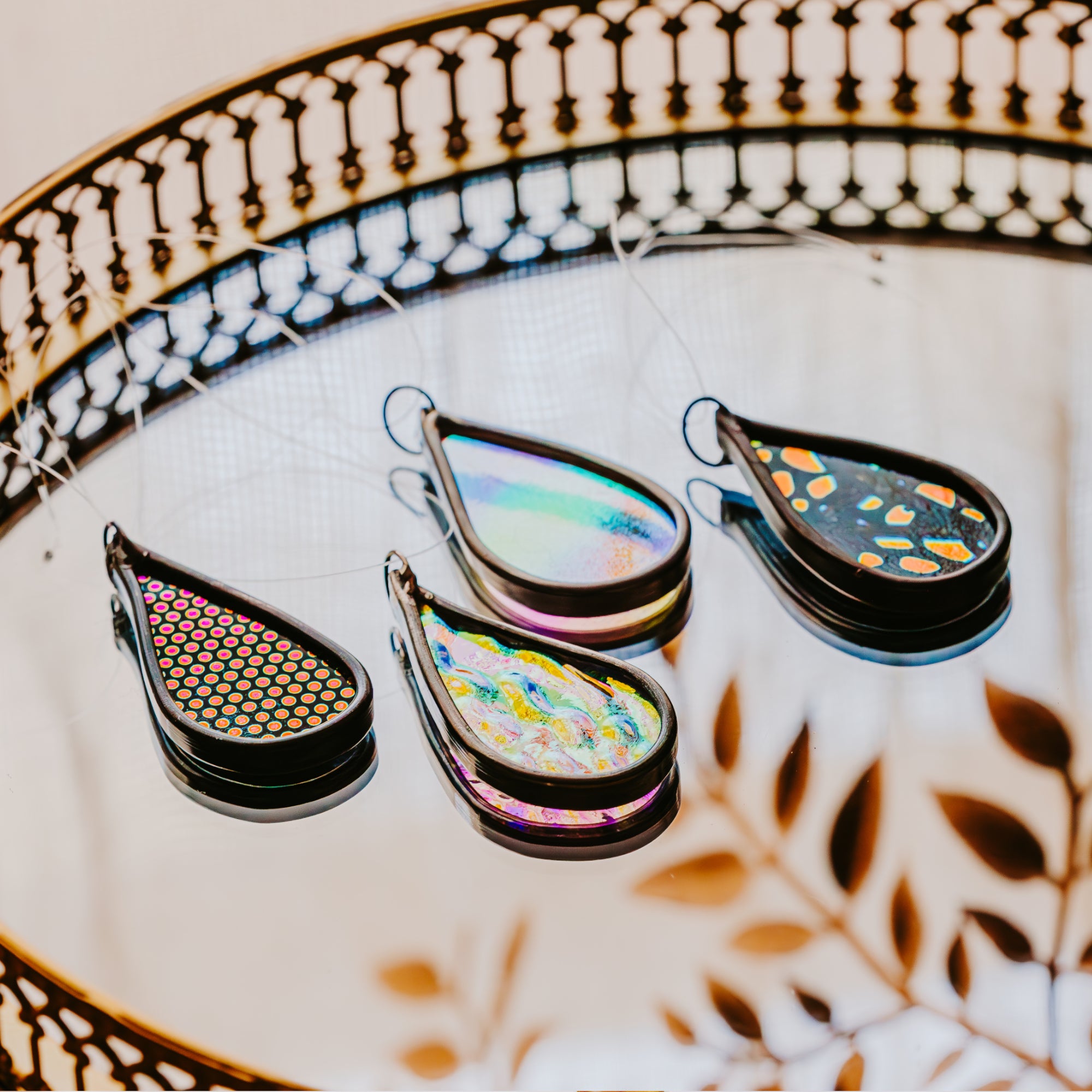Four colorful teardrop-shaped car charms on a decorative mirror with a leaf pattern.
