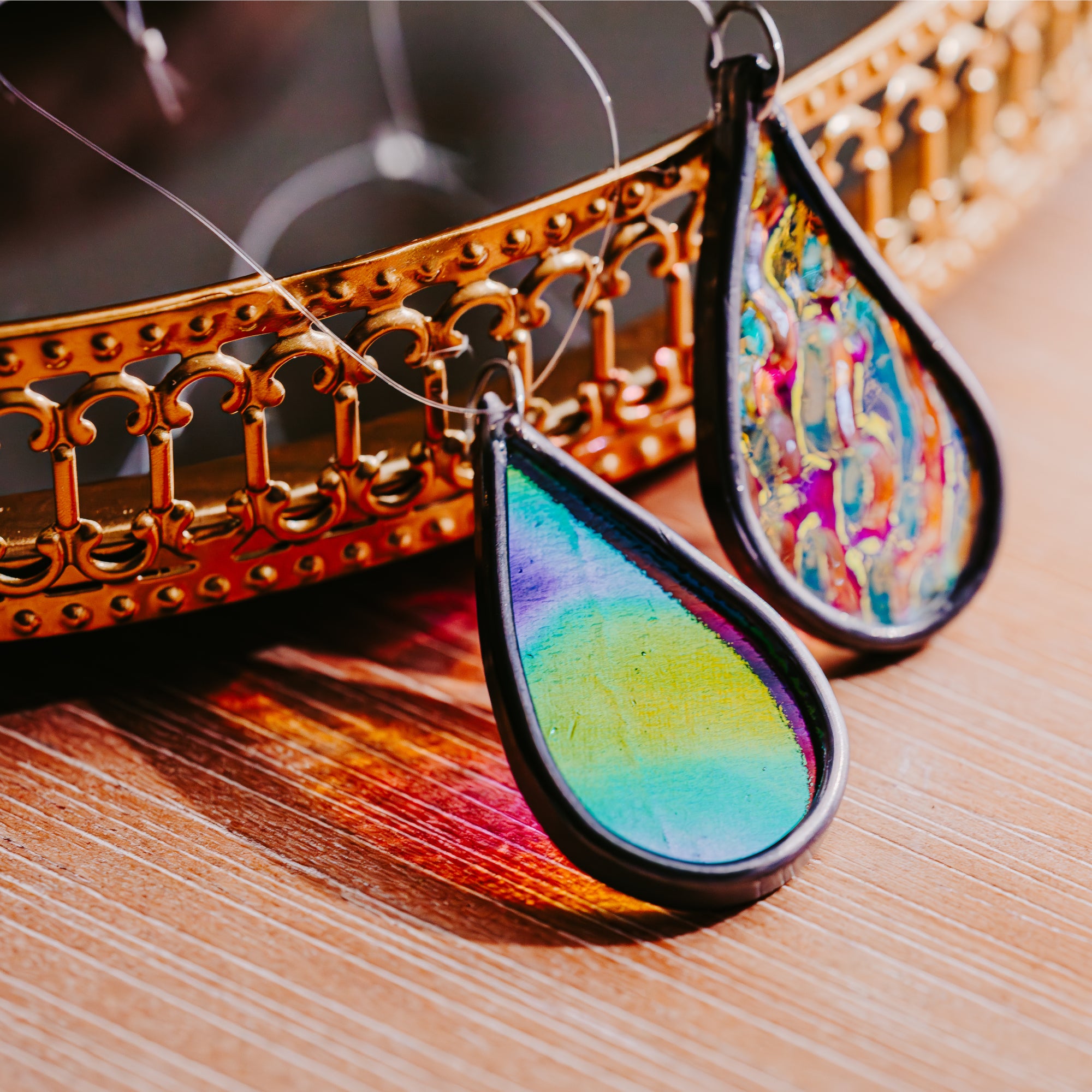 Colorful teardrop-shaped car charms on a wooden surface with a decorative gold frame.