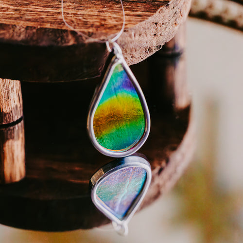 Teardrop-shaped car charm with multicolored design reflected on a mirrored surface
