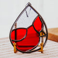 Tear drop-shaped stained glass cardinal suncatcher on a light wooden surface.