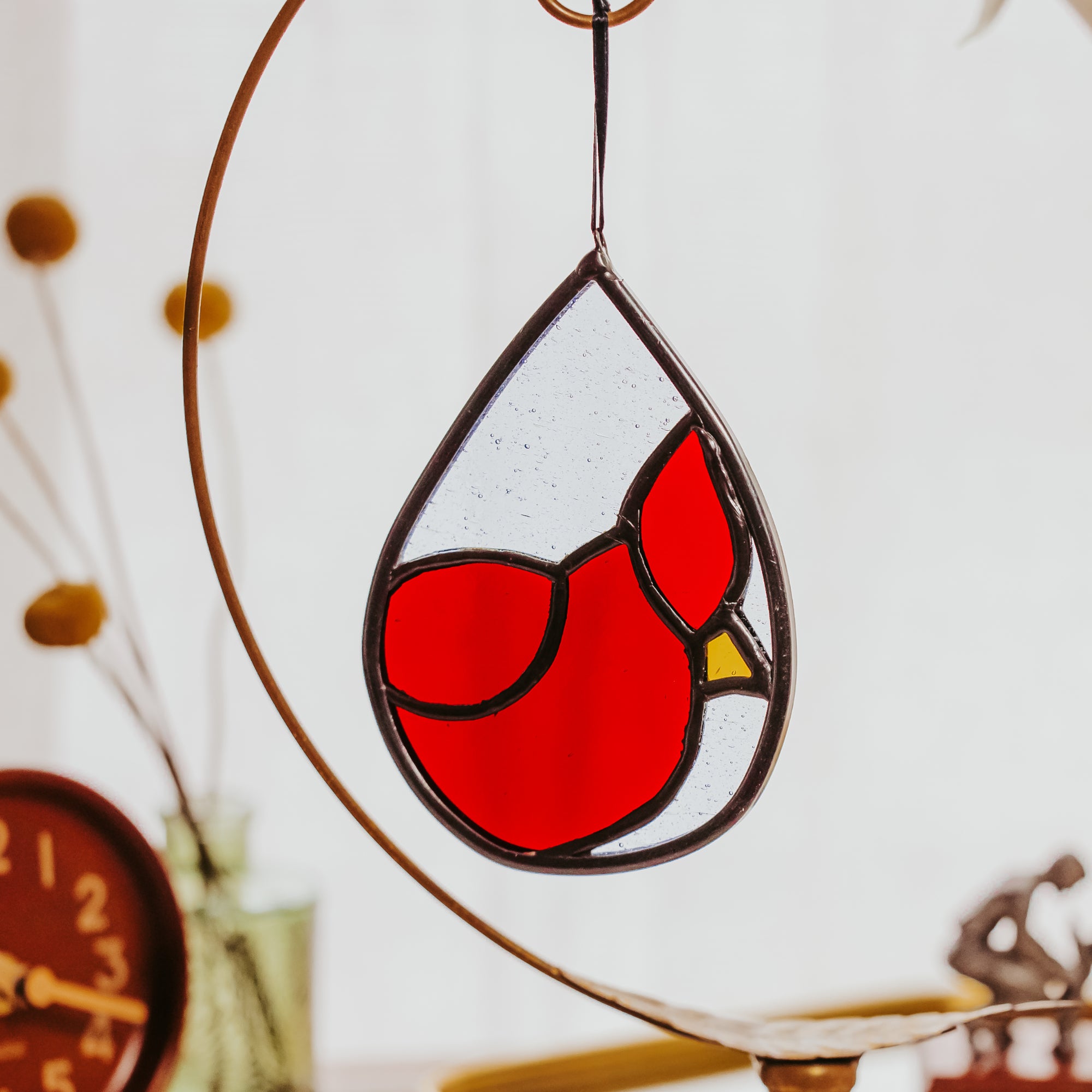Stained glass red bird cardinal design hanging on a white wall with decorative elements in the background