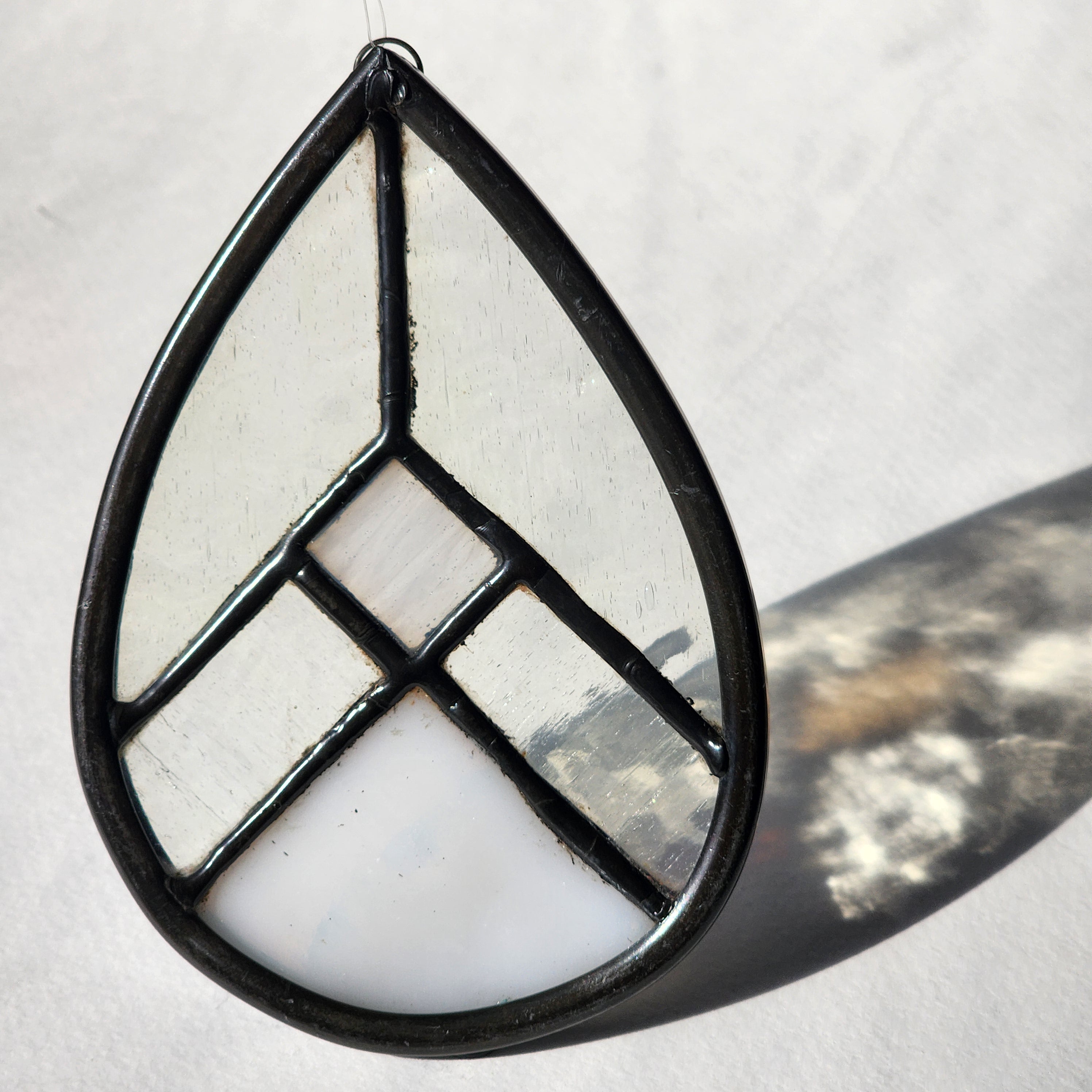 White and clear geometric stained glass suncatcher with transmitted light on a neutral background