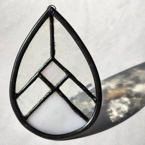 White and clear geometric stained glass suncatcher with transmitted light on a neutral background