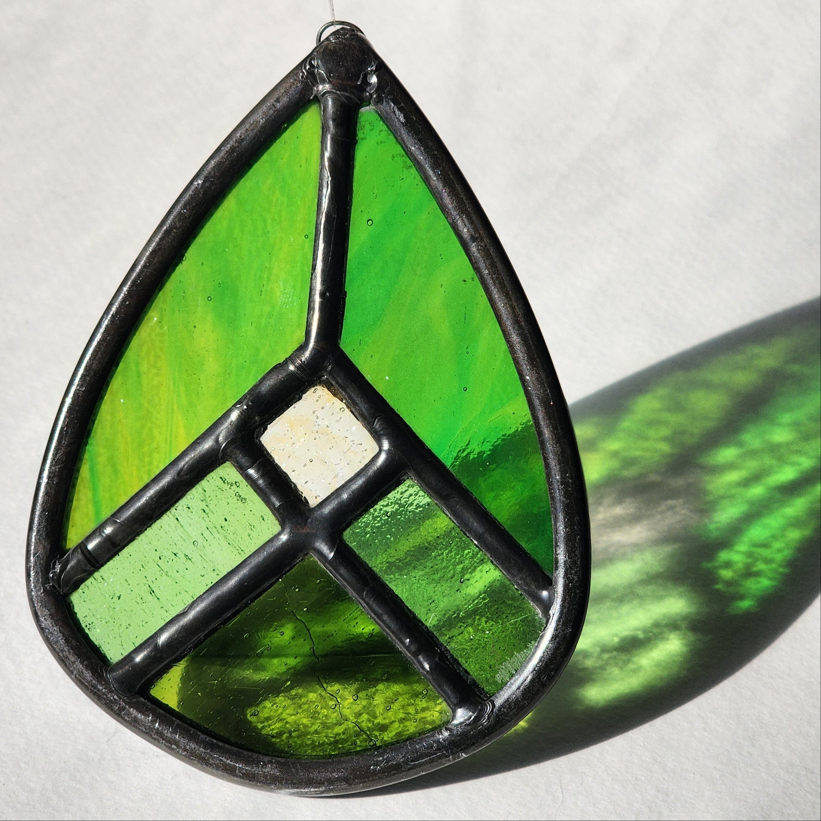 Green geometric stained glass suncatcher with transmitted light on a neutral background