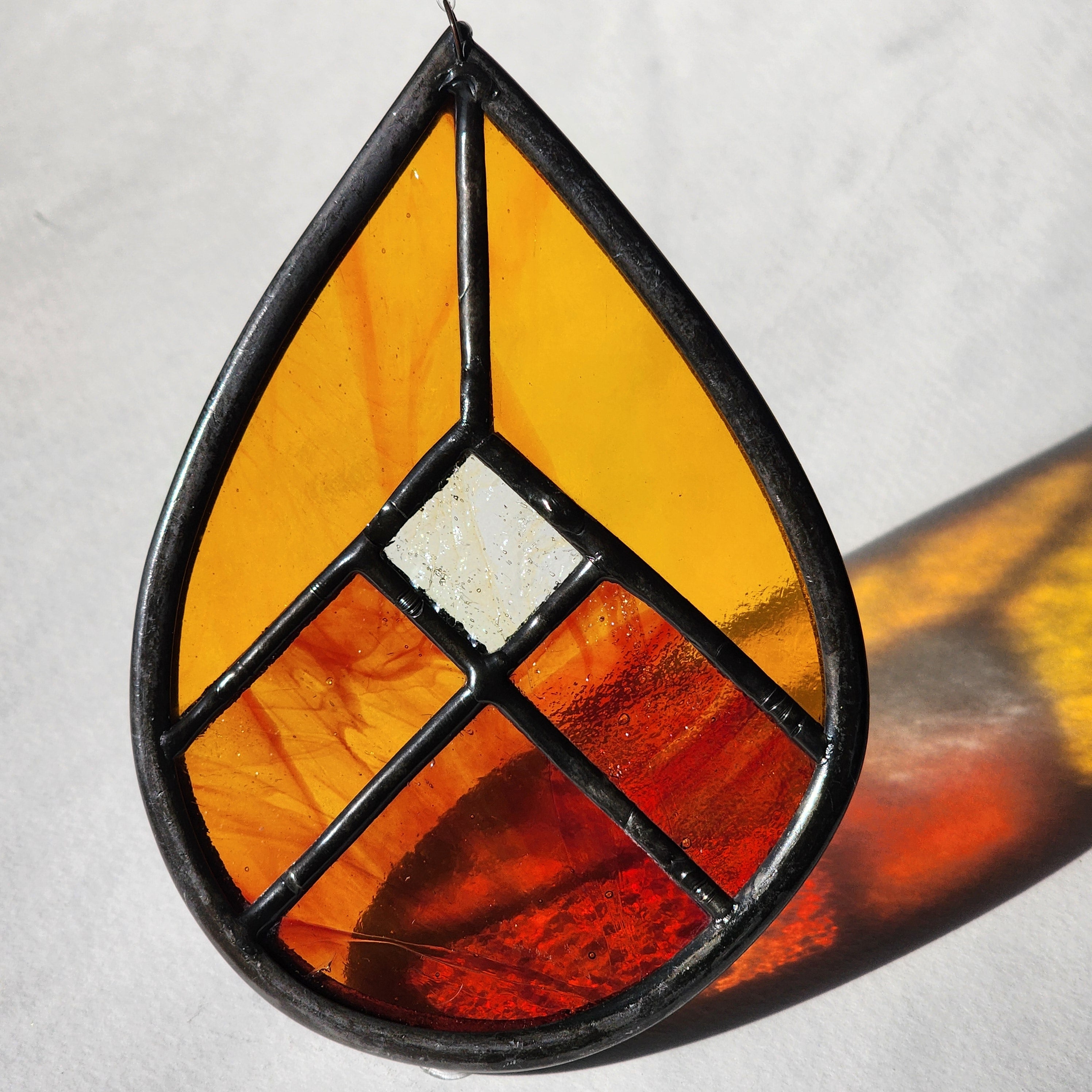 Red and orange geometric stained glass suncatcher with transmitted light on a neutral background