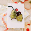 Stained glass Christmas Holly ornament in green wispy, red cathedral (transparent) glass, and wire details on a holiday background