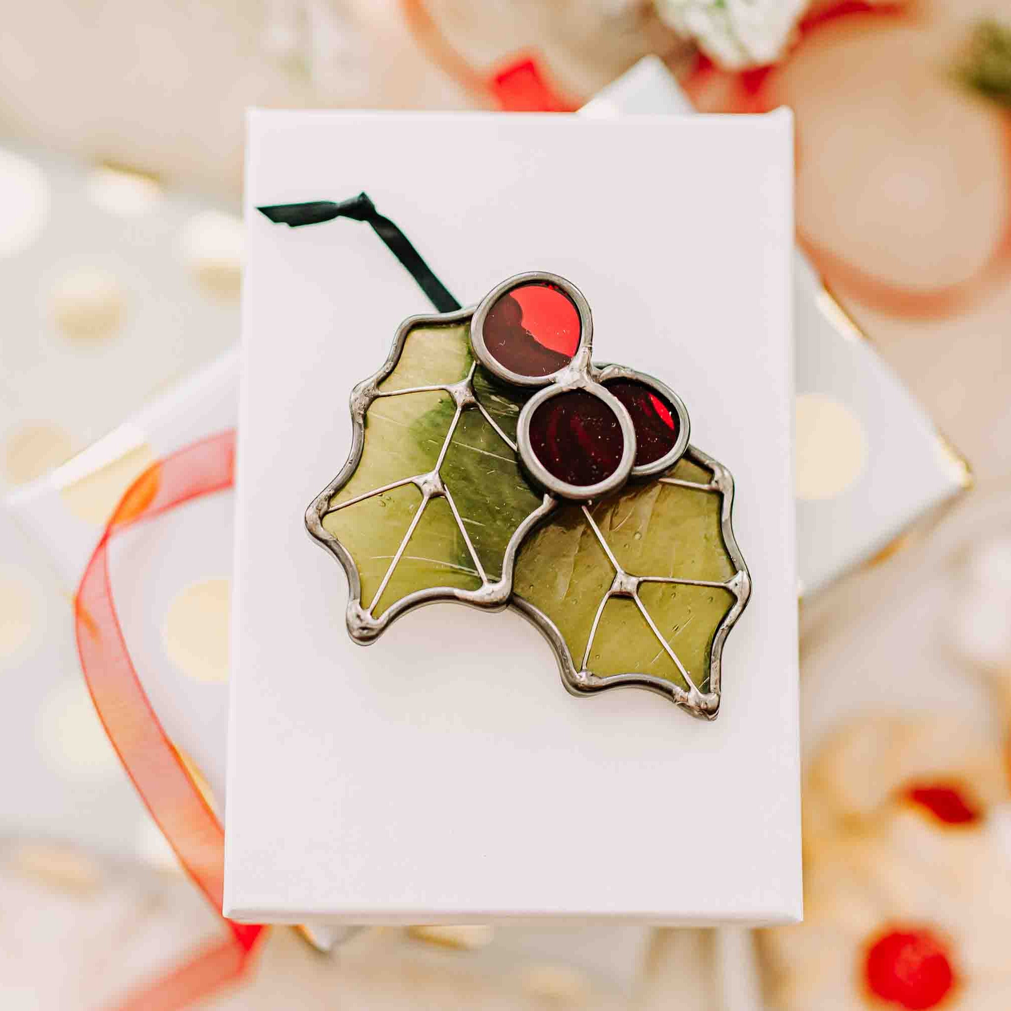 Stained glass Christmas Holly ornament in green wispy, red cathedral (transparent) glass, and wire details on a holiday background