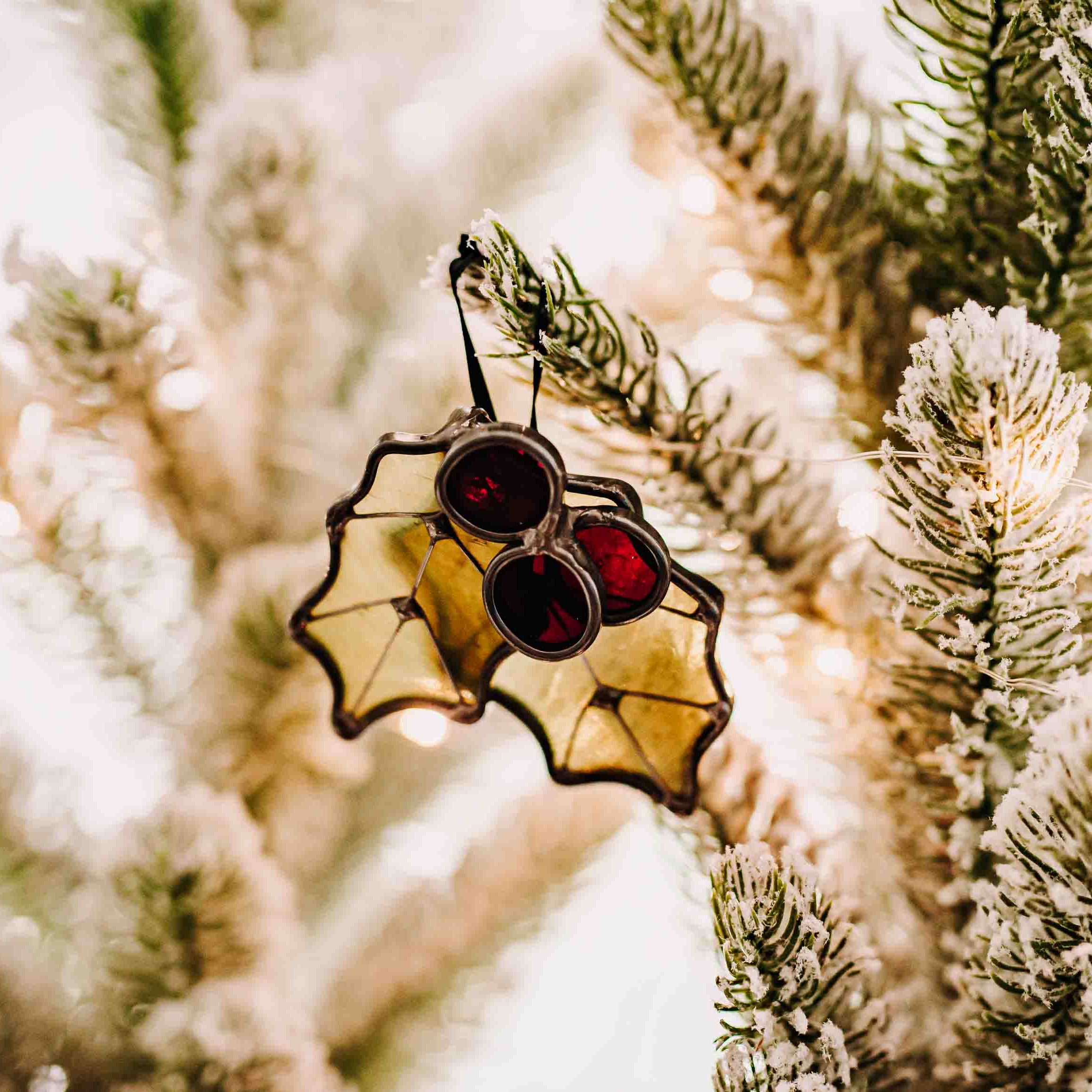 Stained glass Christmas Holly ornament in green wispy, red cathedral (transparent) glass, and wire details on a Christmas tree branch