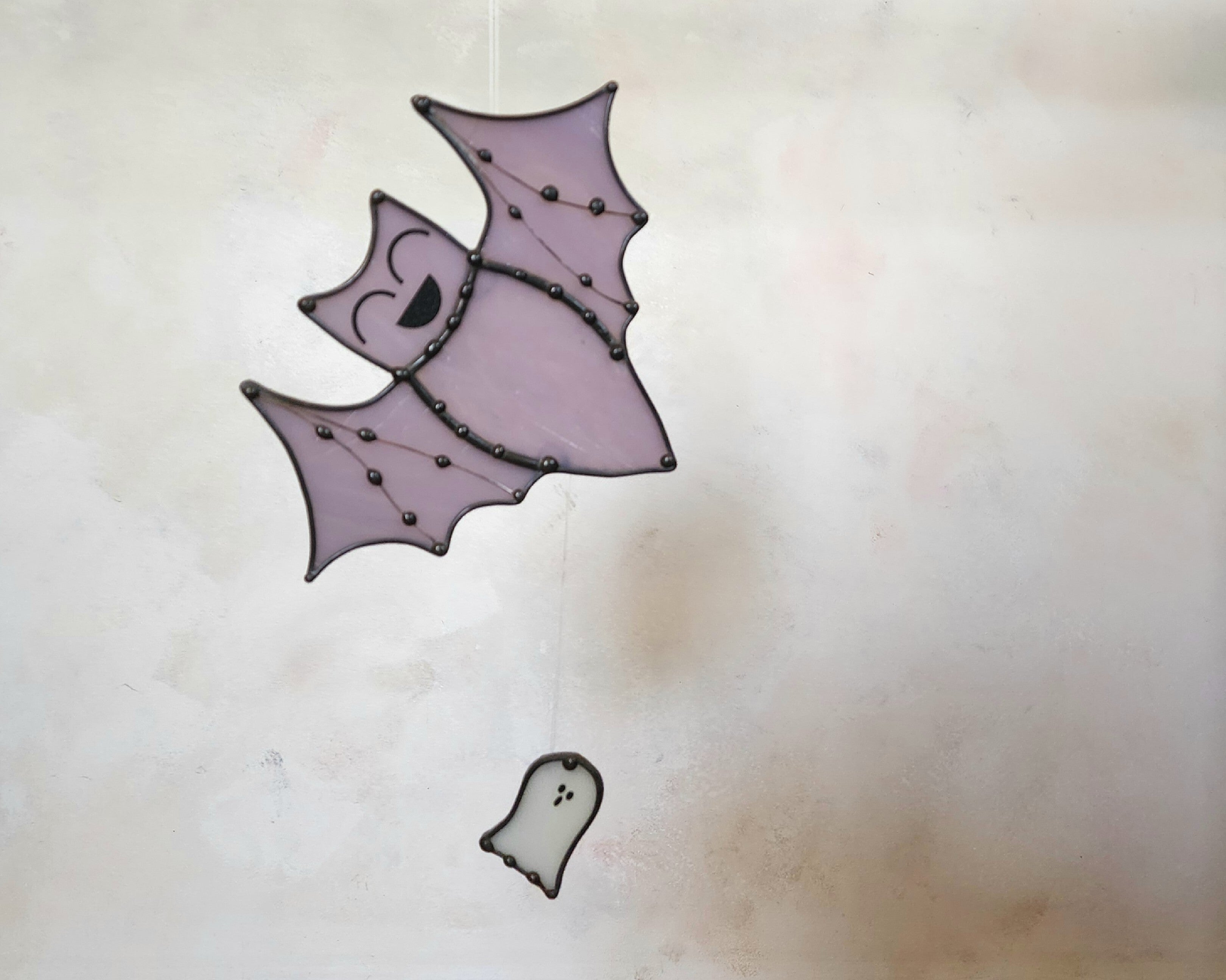 Whimsical purple bat and white ghost stained glass suncatcher on neutral background