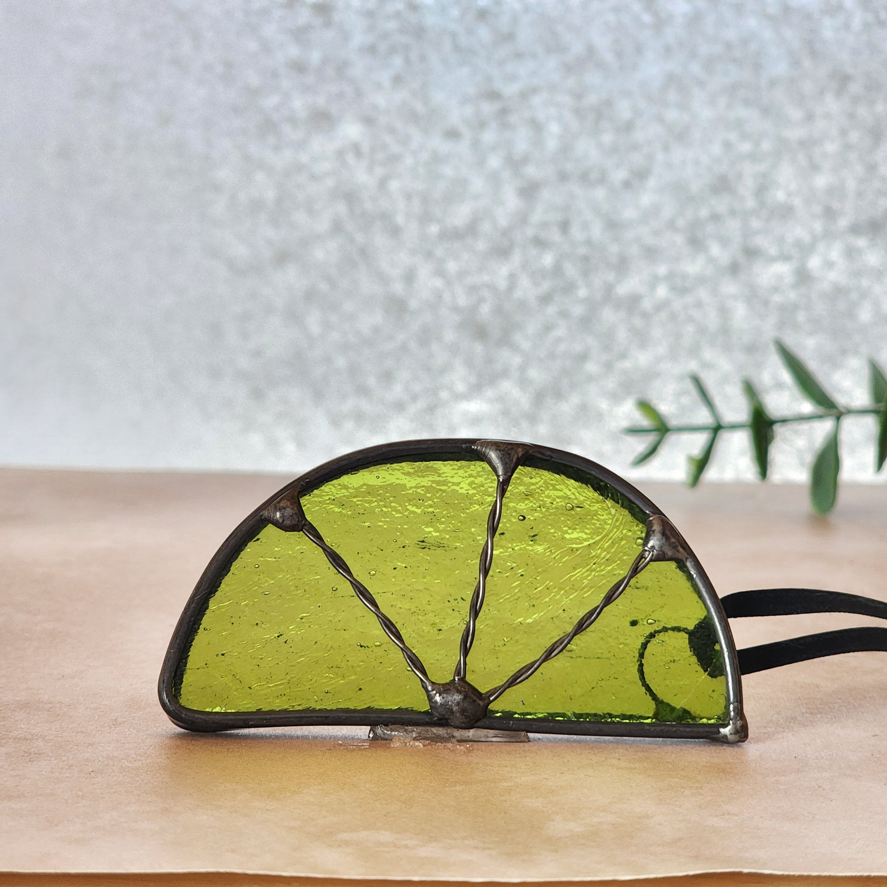 Lime wedge suncatcher made from lightly textured green art glass on a wooden surface with a light background