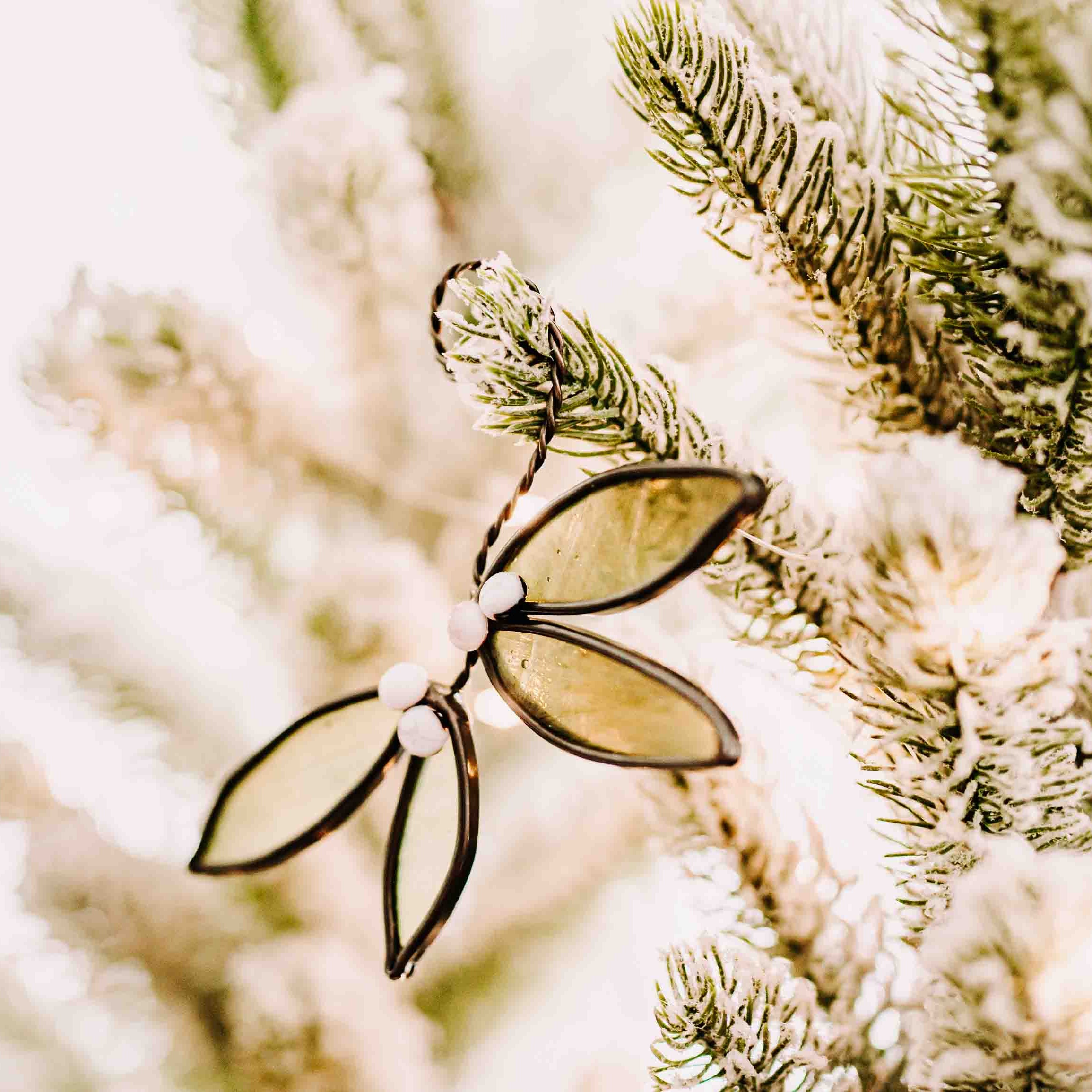 Green stained glass mistletoe with white fused glass berries and hand-twisted wire stem on holiday background