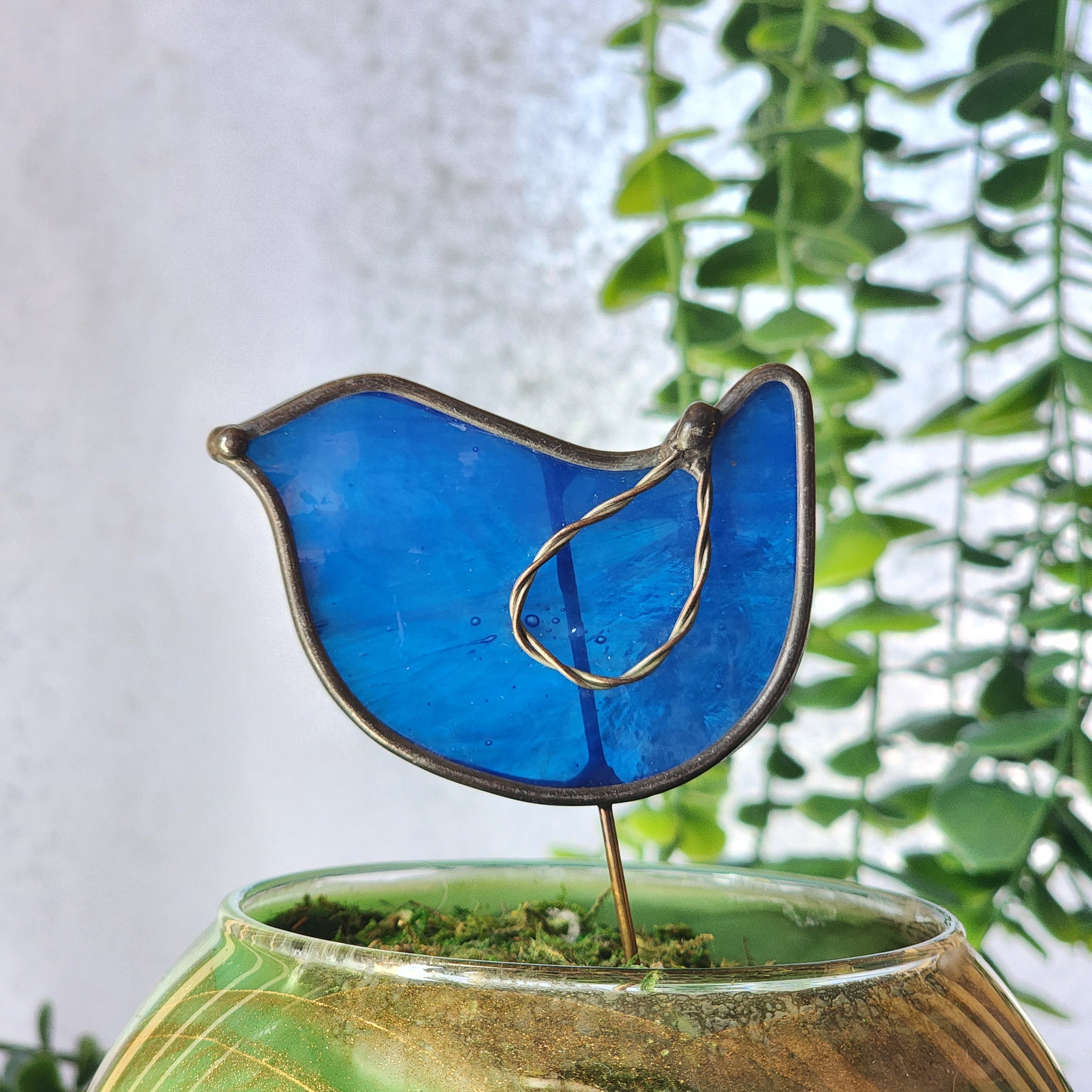 Blue bird plant stake against a green leafy background