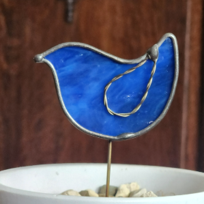 Blue glass bird ornament on a stand with a wooden background