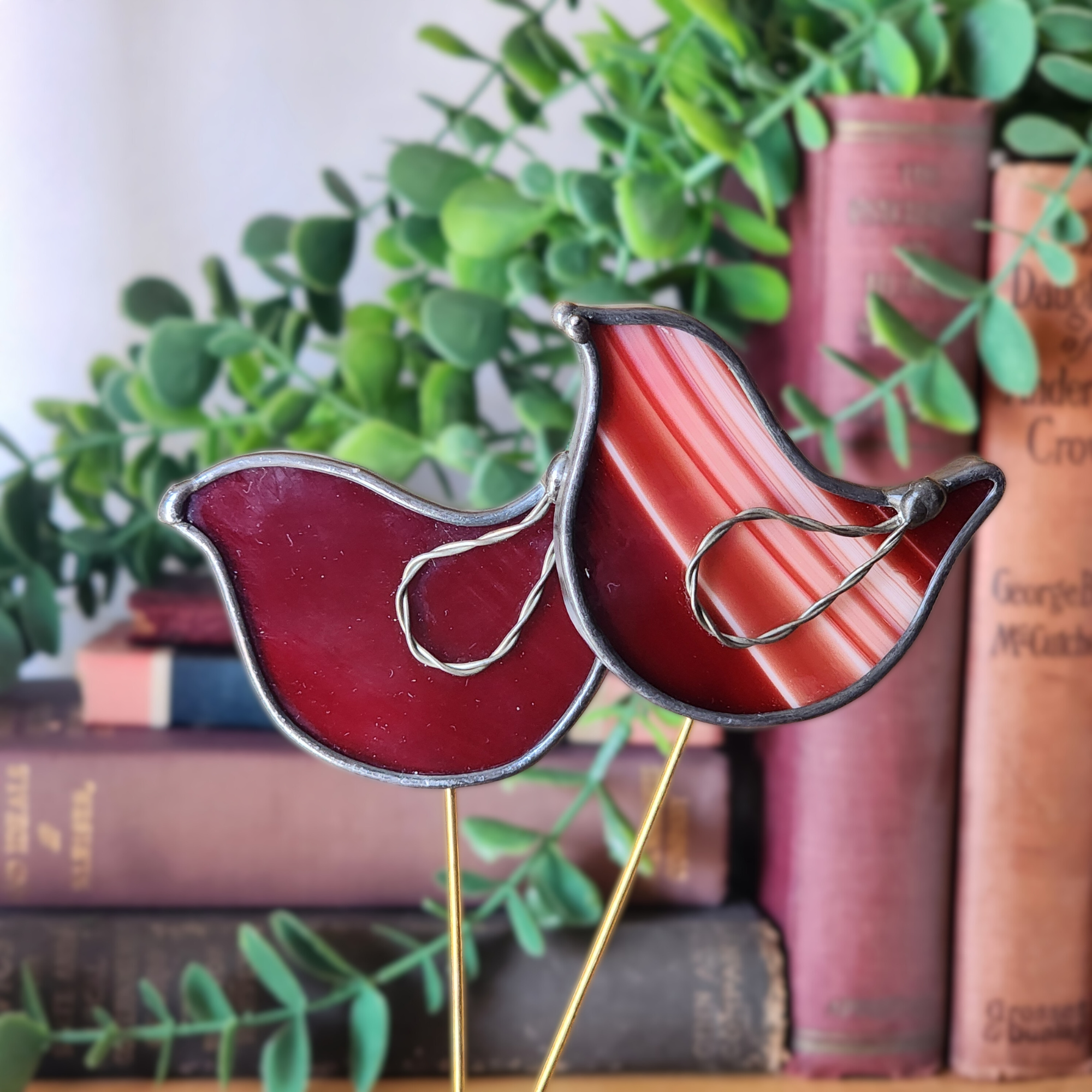 Decorative red bird ornament on a stick with books and greenery in the background