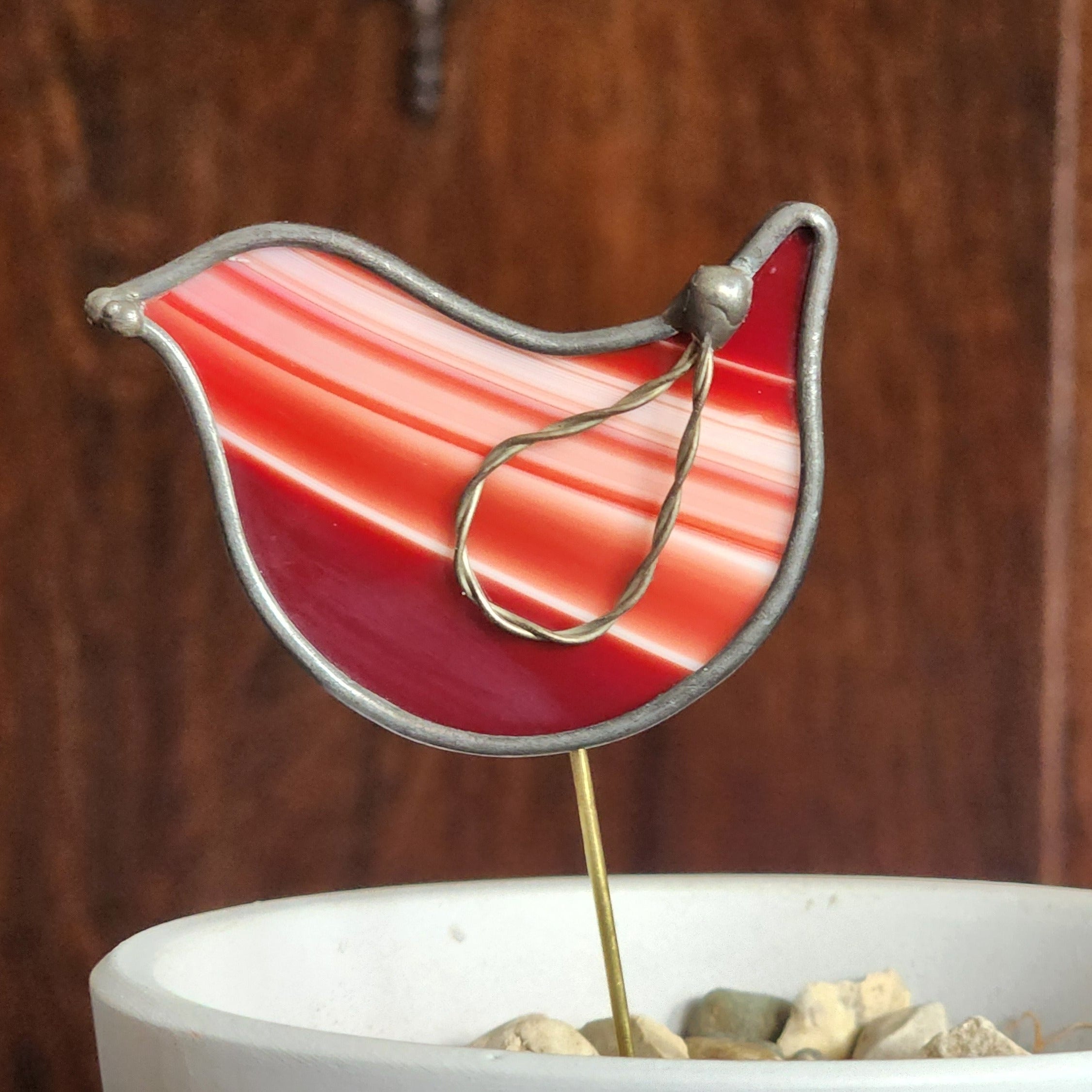 Decorative red glass bird on a stand with a wooden background