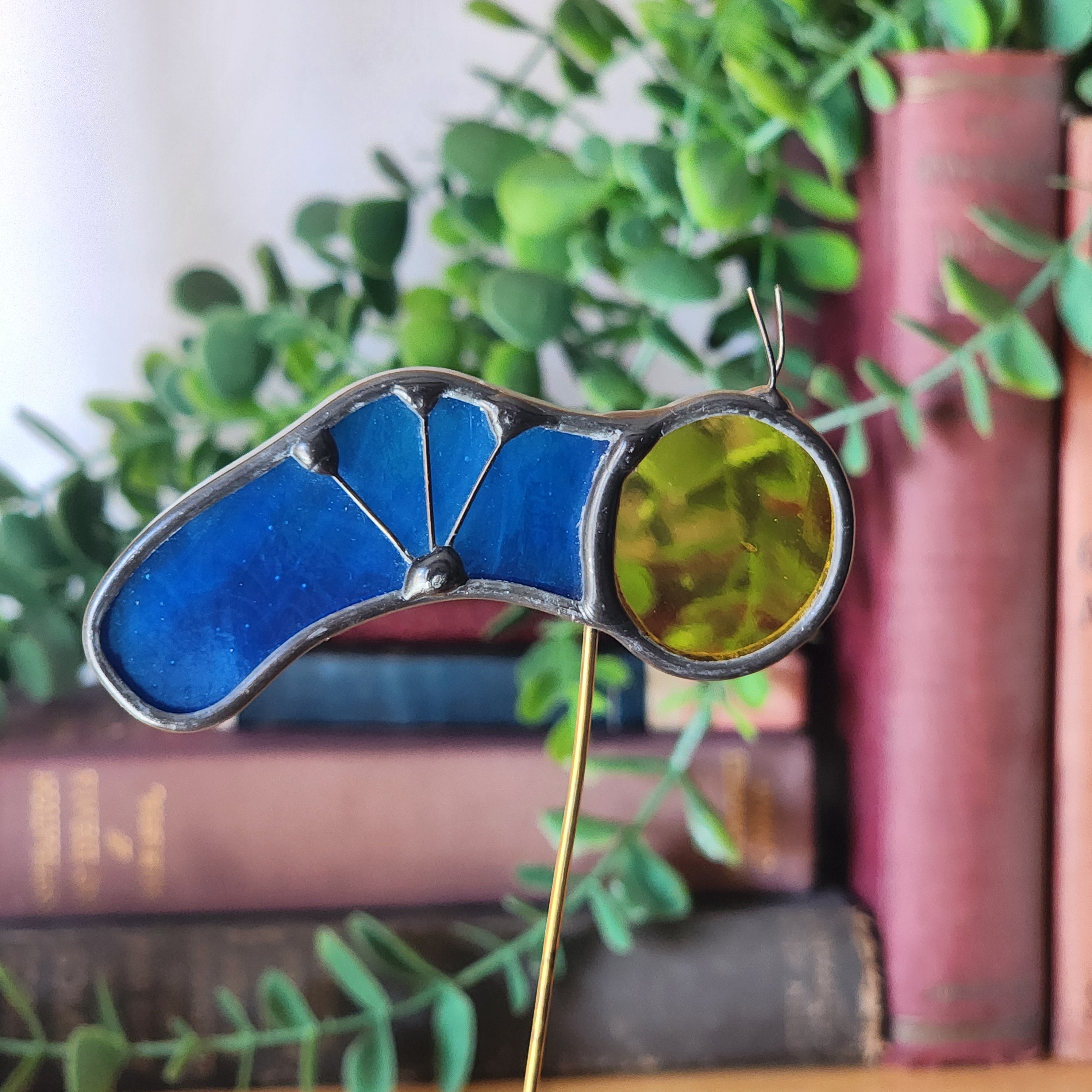 Caterpillar stained glass ornament with blue and green body on a blurred bookshelf background.