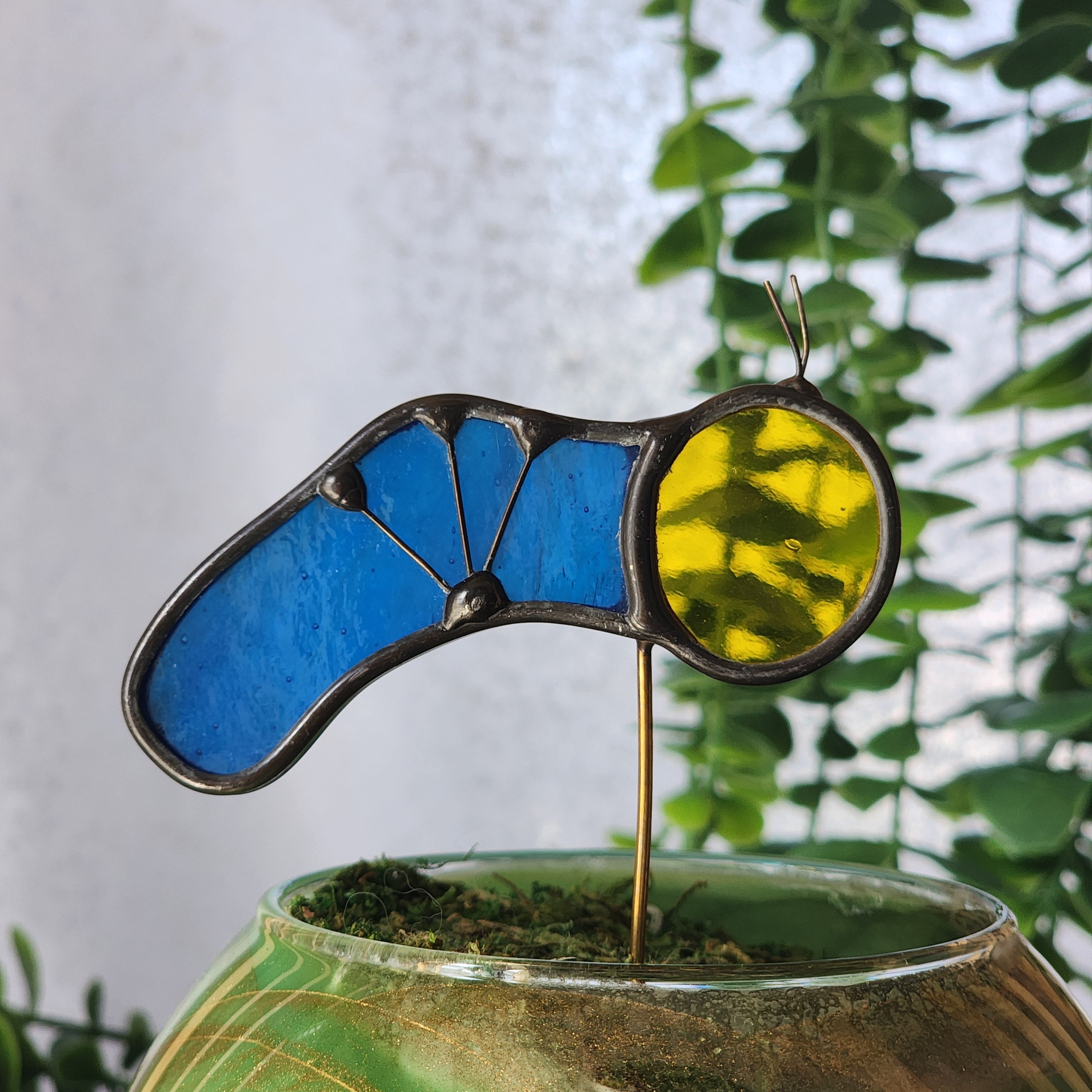 Stained glass caterpillar with blue and yellow body tucked in to a plant