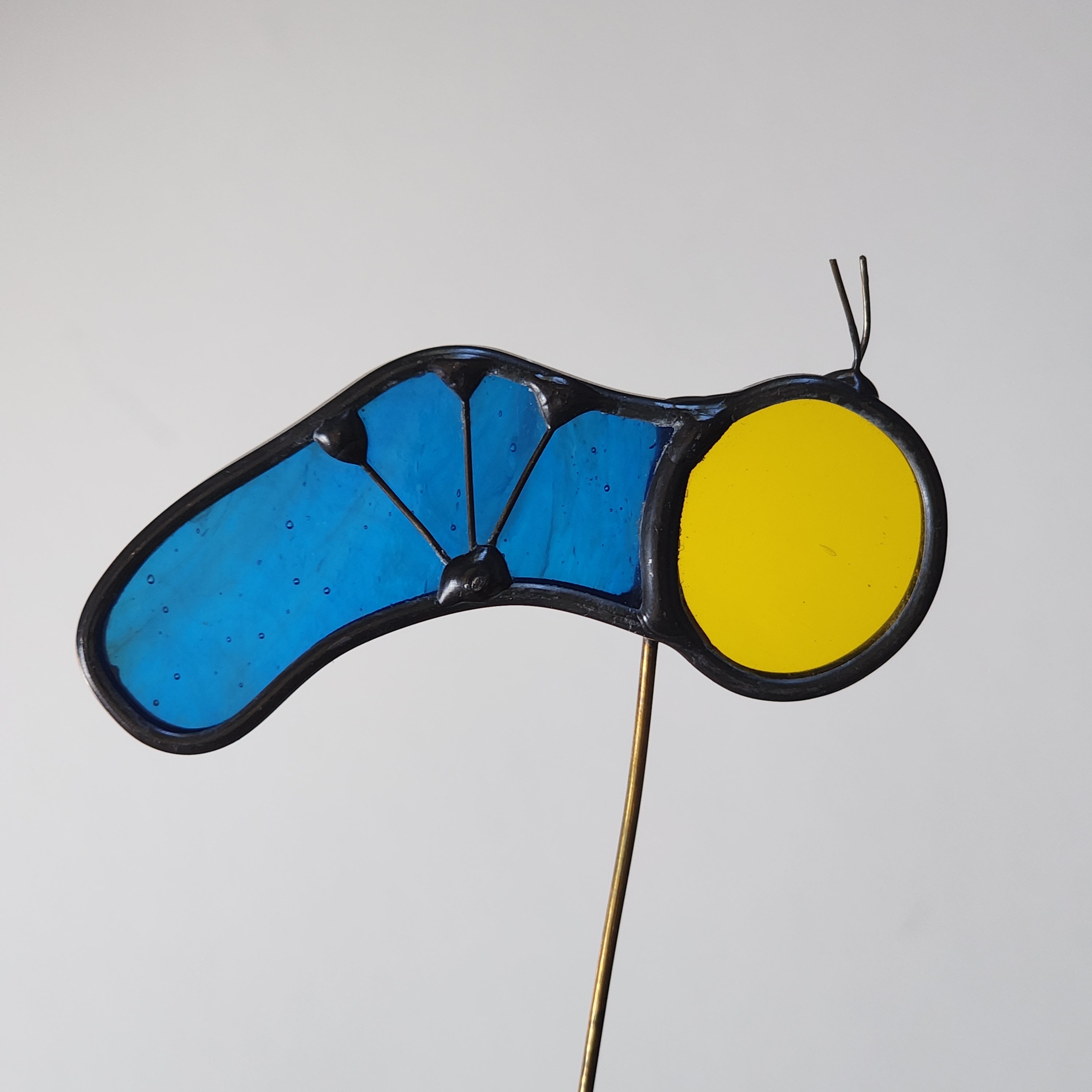 Yellow and blue stained glass caterpillar plant stake on a white background
