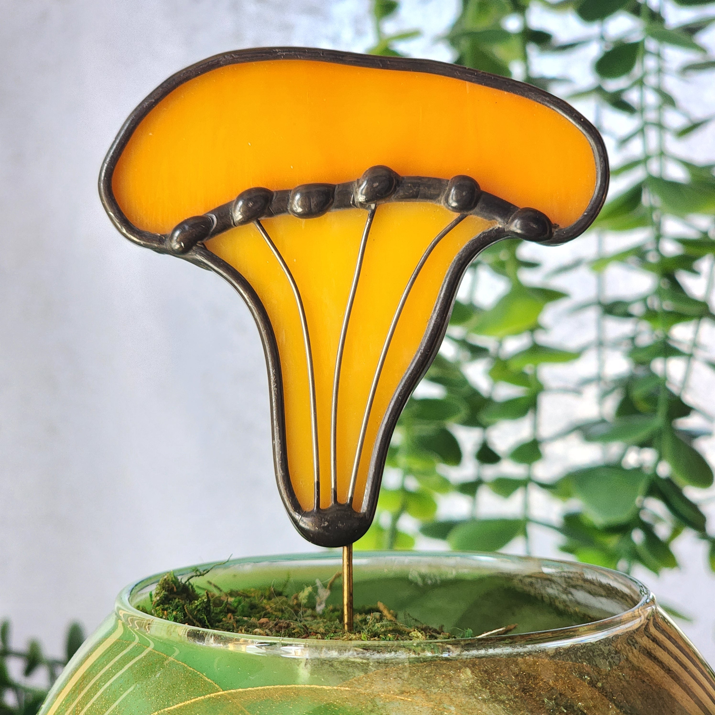 Close-up of a Chanterelle stained glass plant stake with green foliage in the background