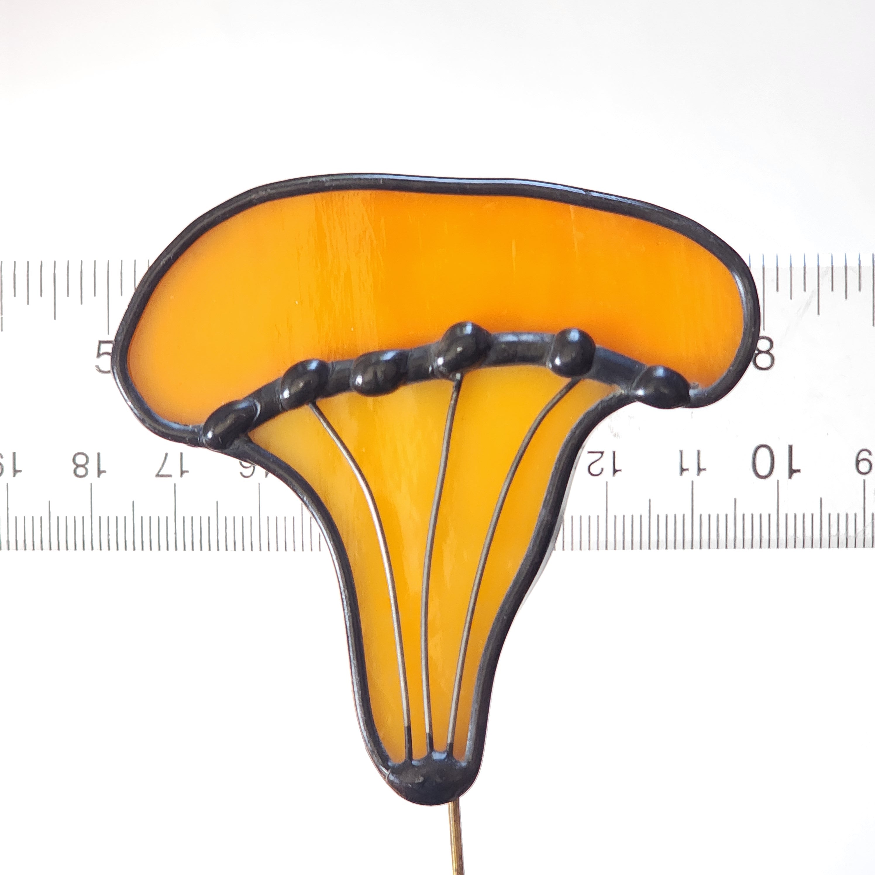 Yellow orange stained glass chanterelle plant stake next to a ruler for scale on a white background