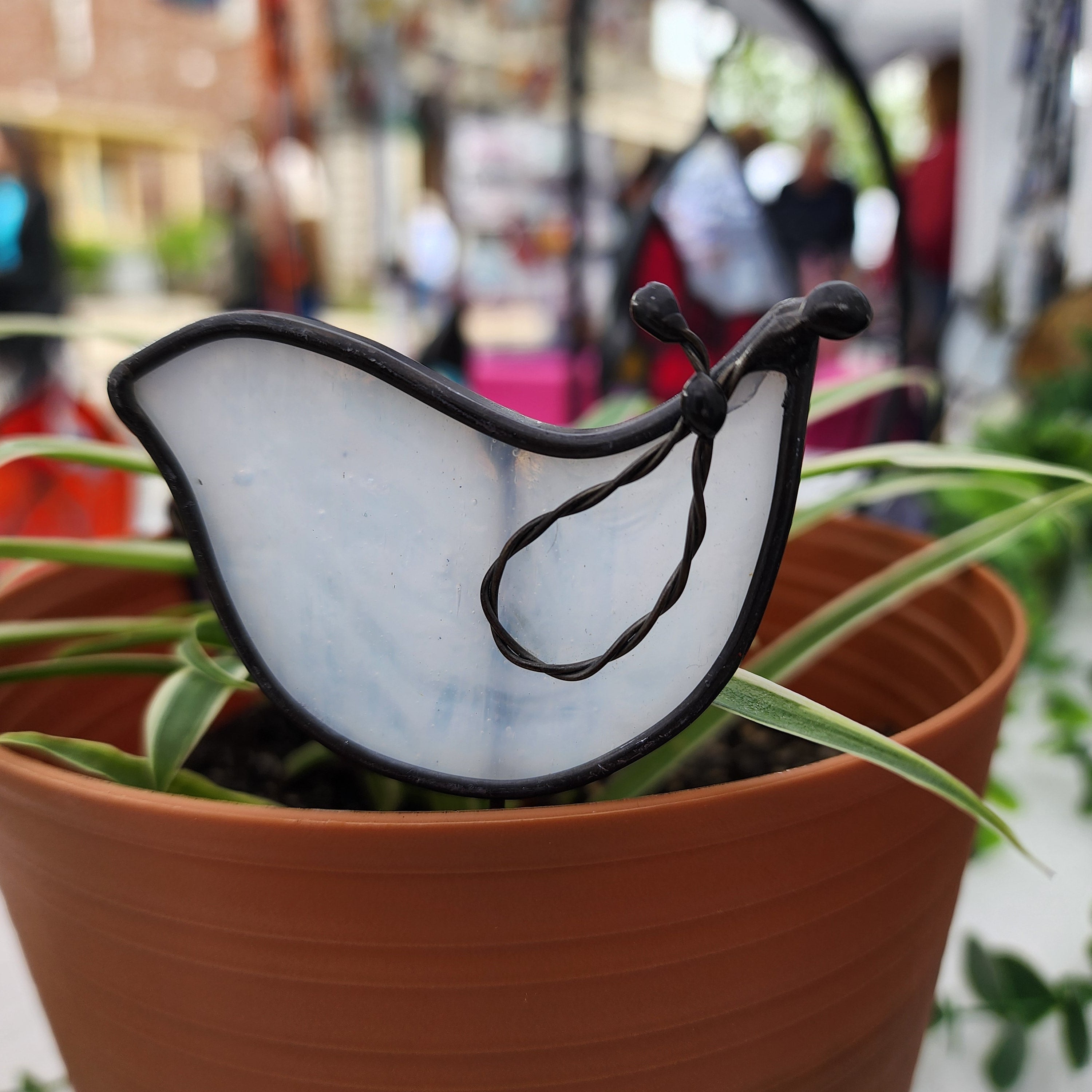 White dove stained glass plant stake in a pot with a blurred setting in the backgroun