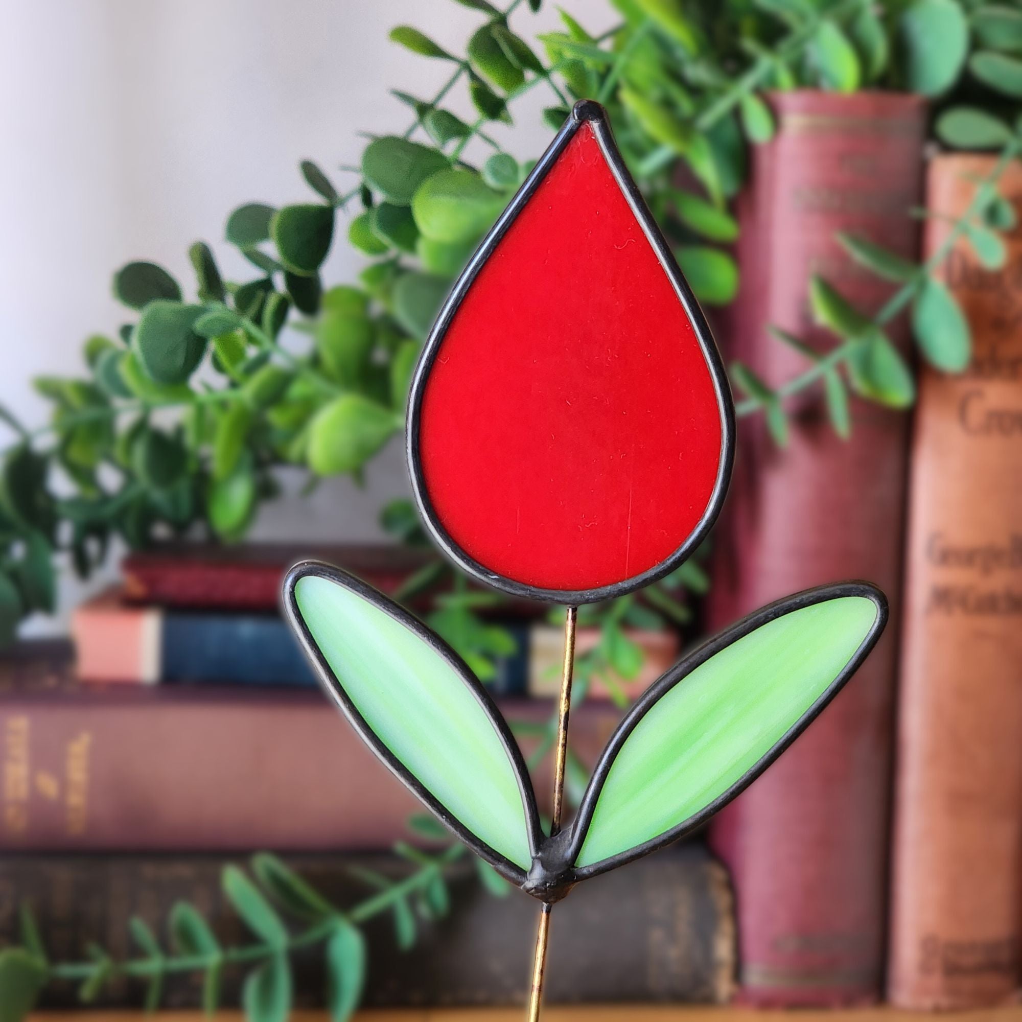 Stained glass red tulip with green leaves on a blurred bookshelf background