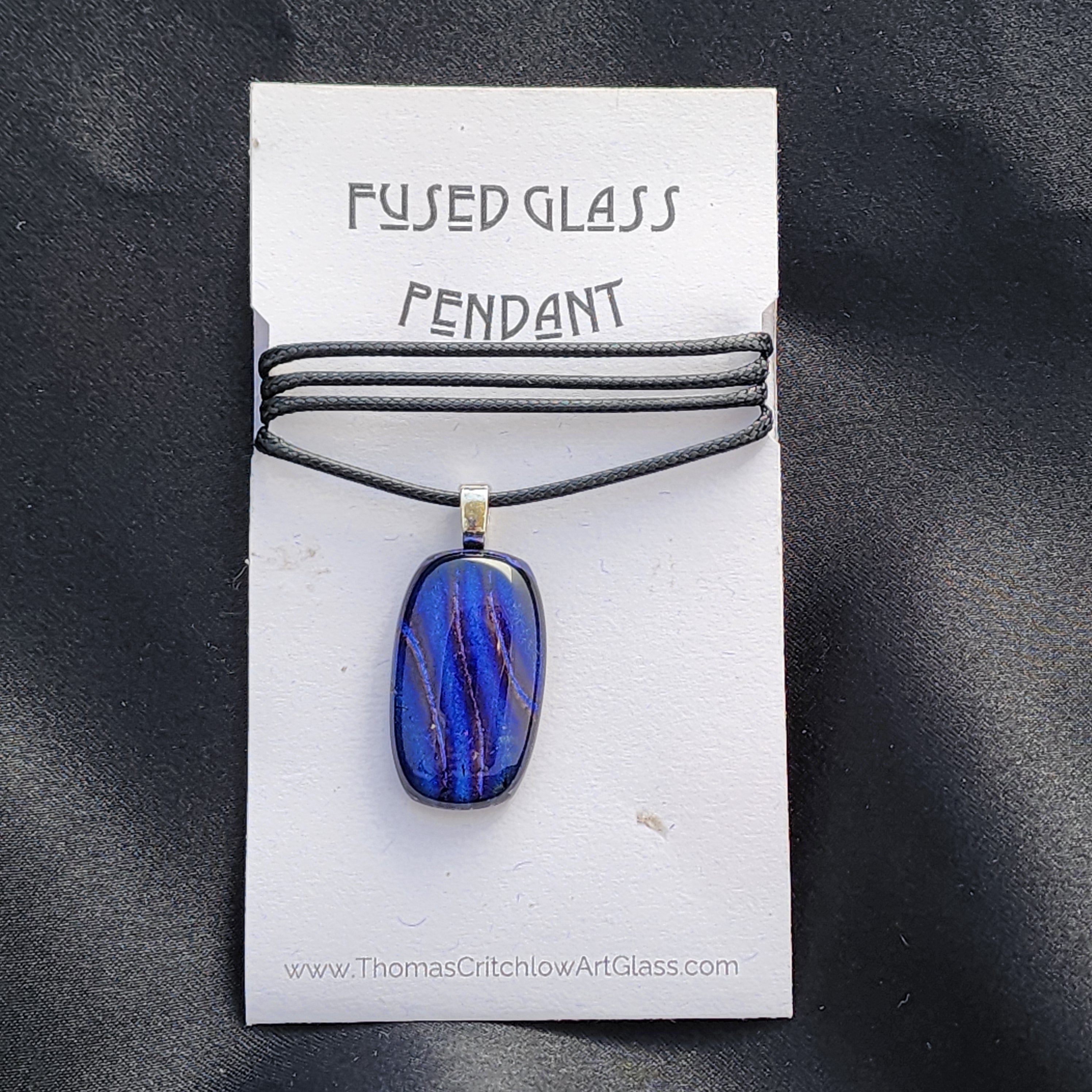 Fused glass pendant on a card with 'Thomas Critchlow Art Glass' branding on a black background