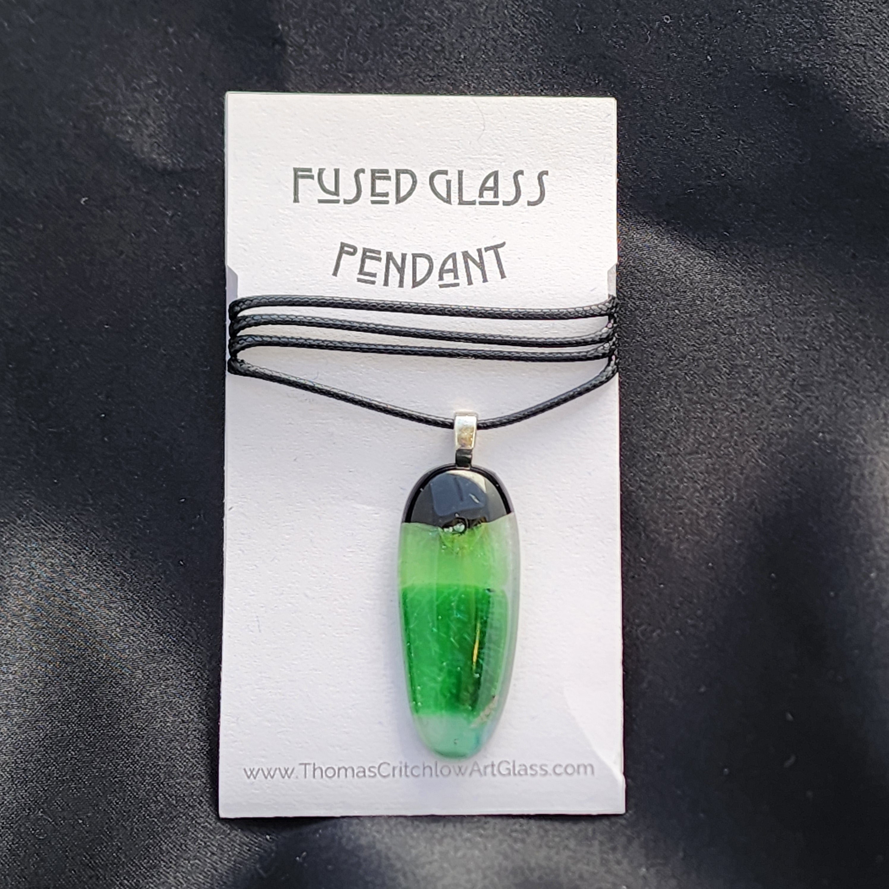 Green fused glass pendant on a card with 'Fused Glass Pendant' text against a black background