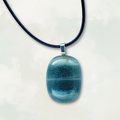 Iridescent blue glass pendant on a black cord against a white background