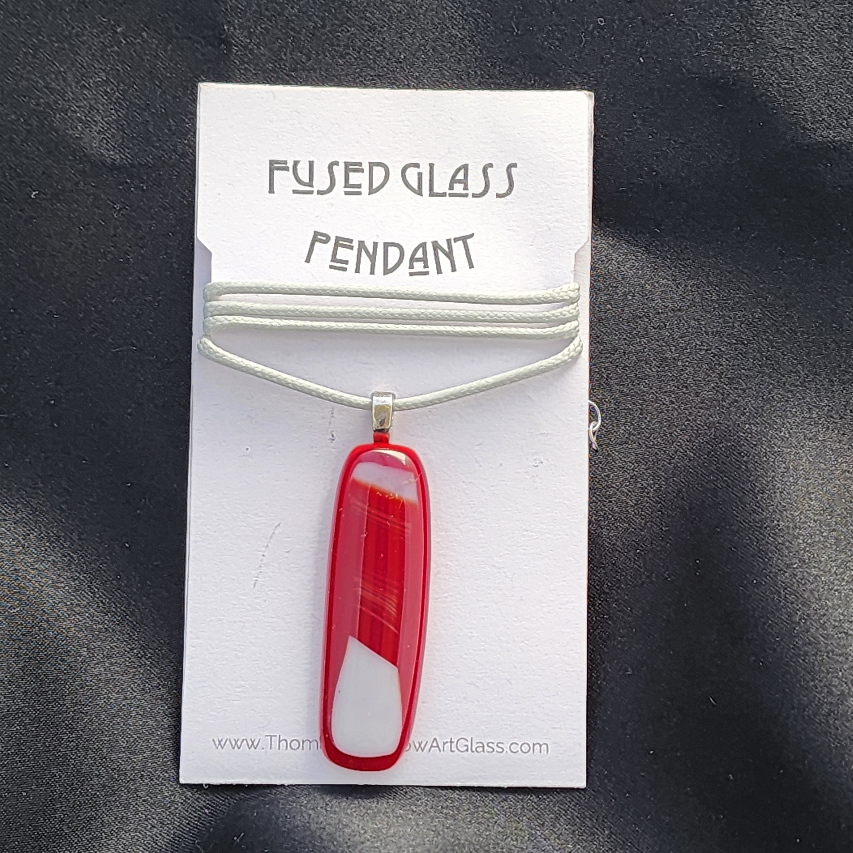 Red fused glass pendant on a white card with text on a black background