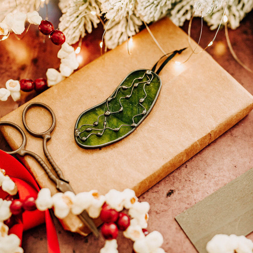 Decorative green stained glass pickle ornament on a wrapped gift with festive background