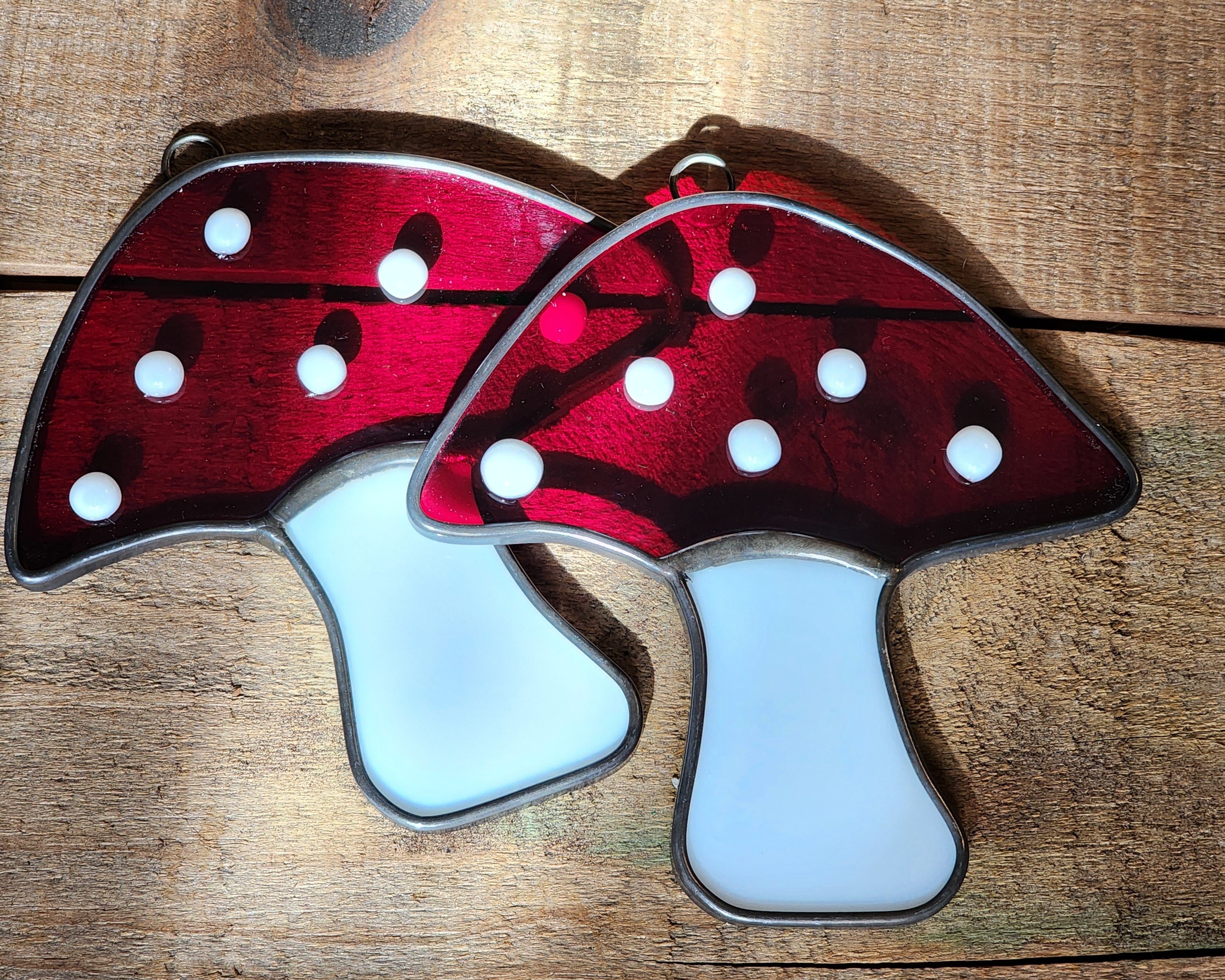 Two stained glass mushrooms with red caps and white spots on a wooden surface