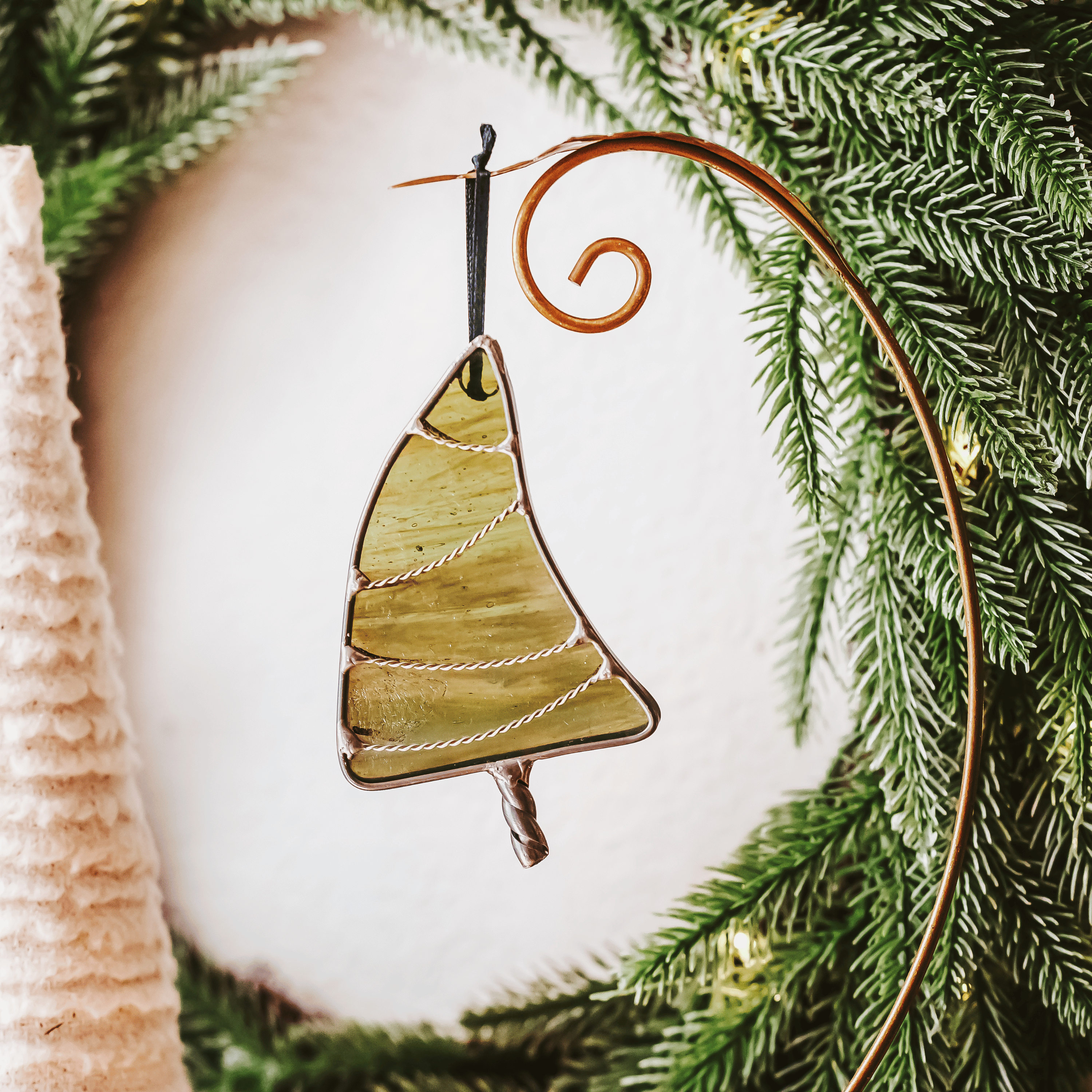 Classic green stained glass Christmas tree ornament with hand twisted metal garland and trunk on a holiday background