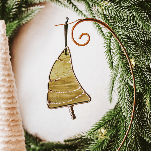 Classic green stained glass Christmas tree ornament with hand twisted metal garland and trunk on a holiday background