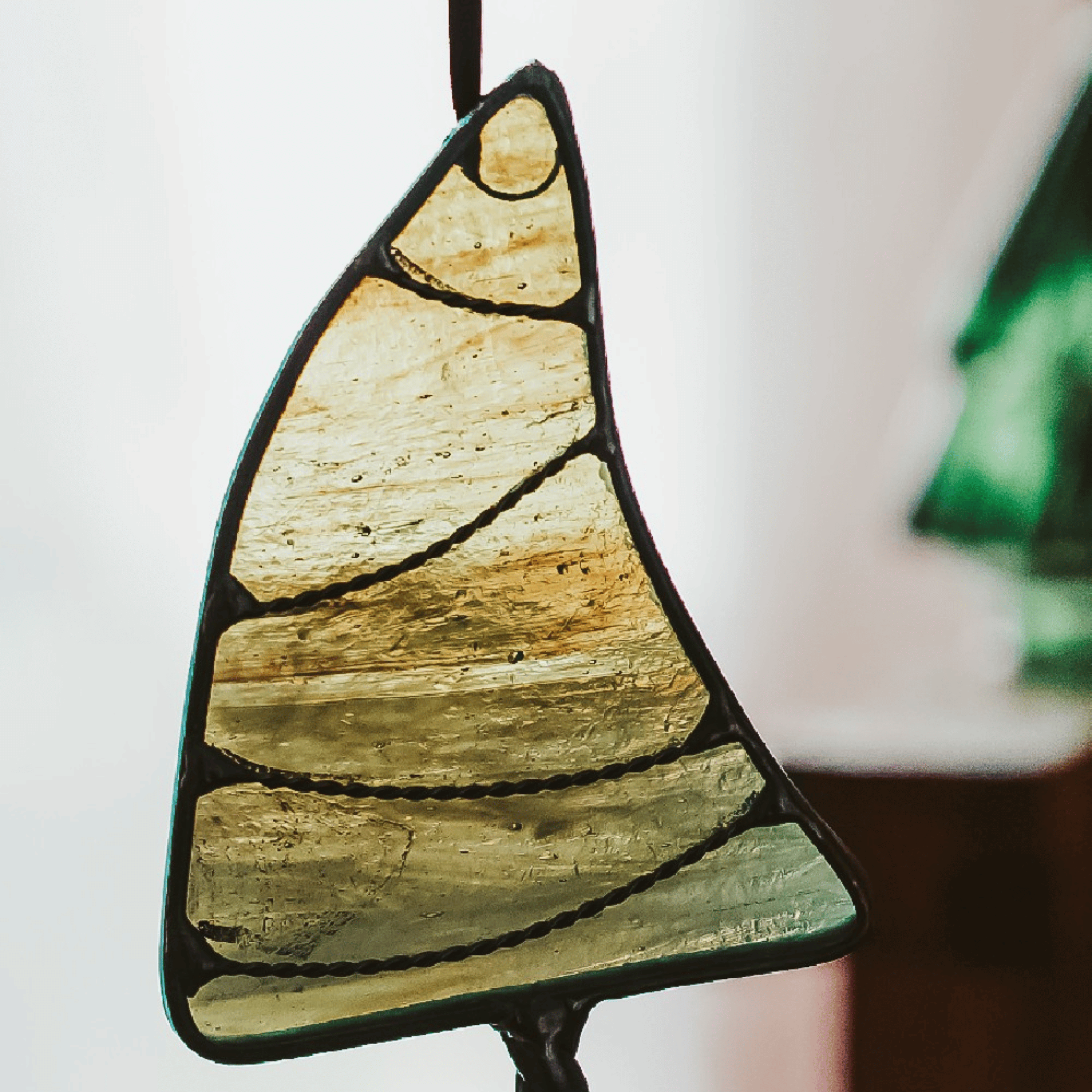 Classic green stained glass Christmas tree ornament with hand twisted metal garland and trunk on a neutral background