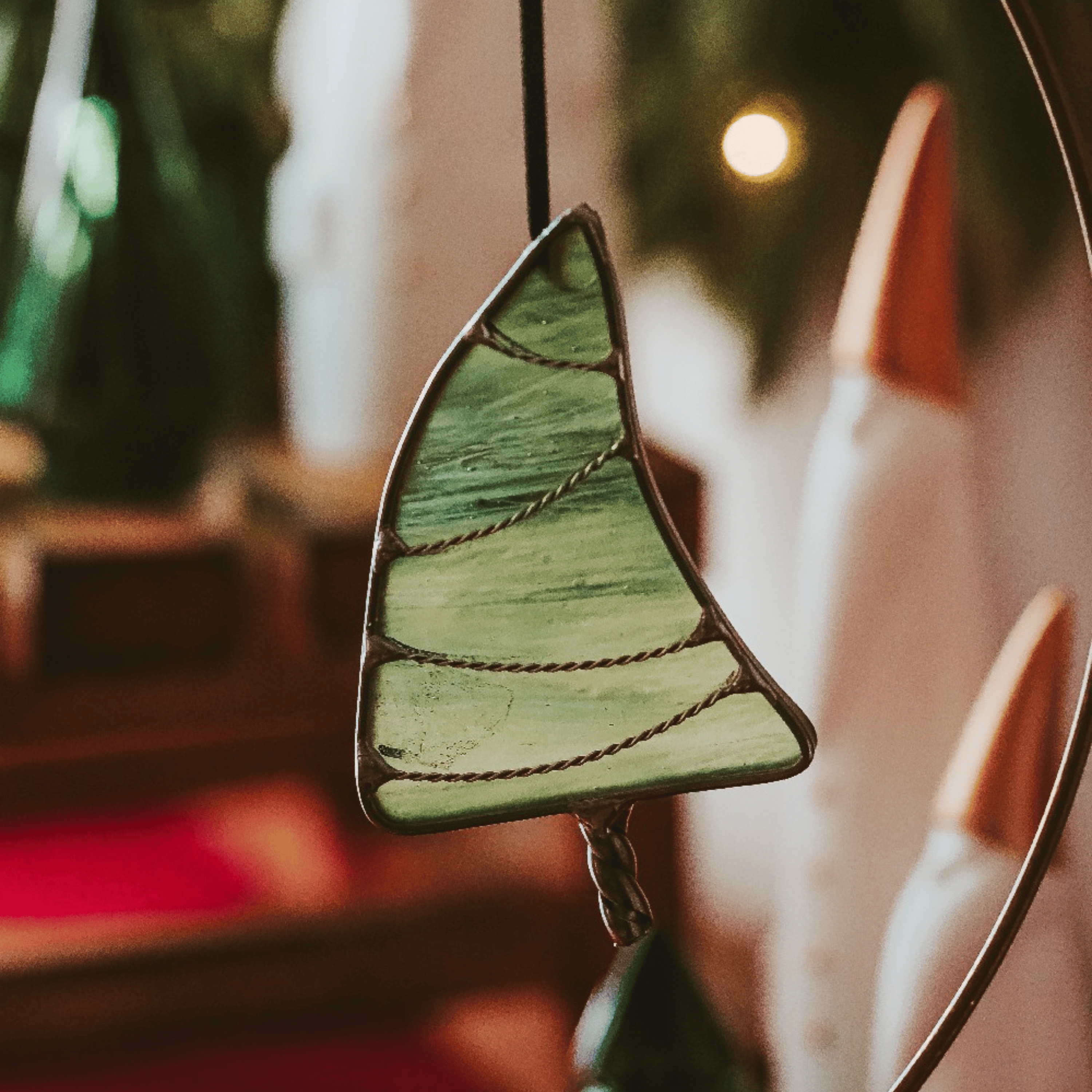 Classic green stained glass Christmas tree ornament with hand twisted metal garland and trunk on a holiday background