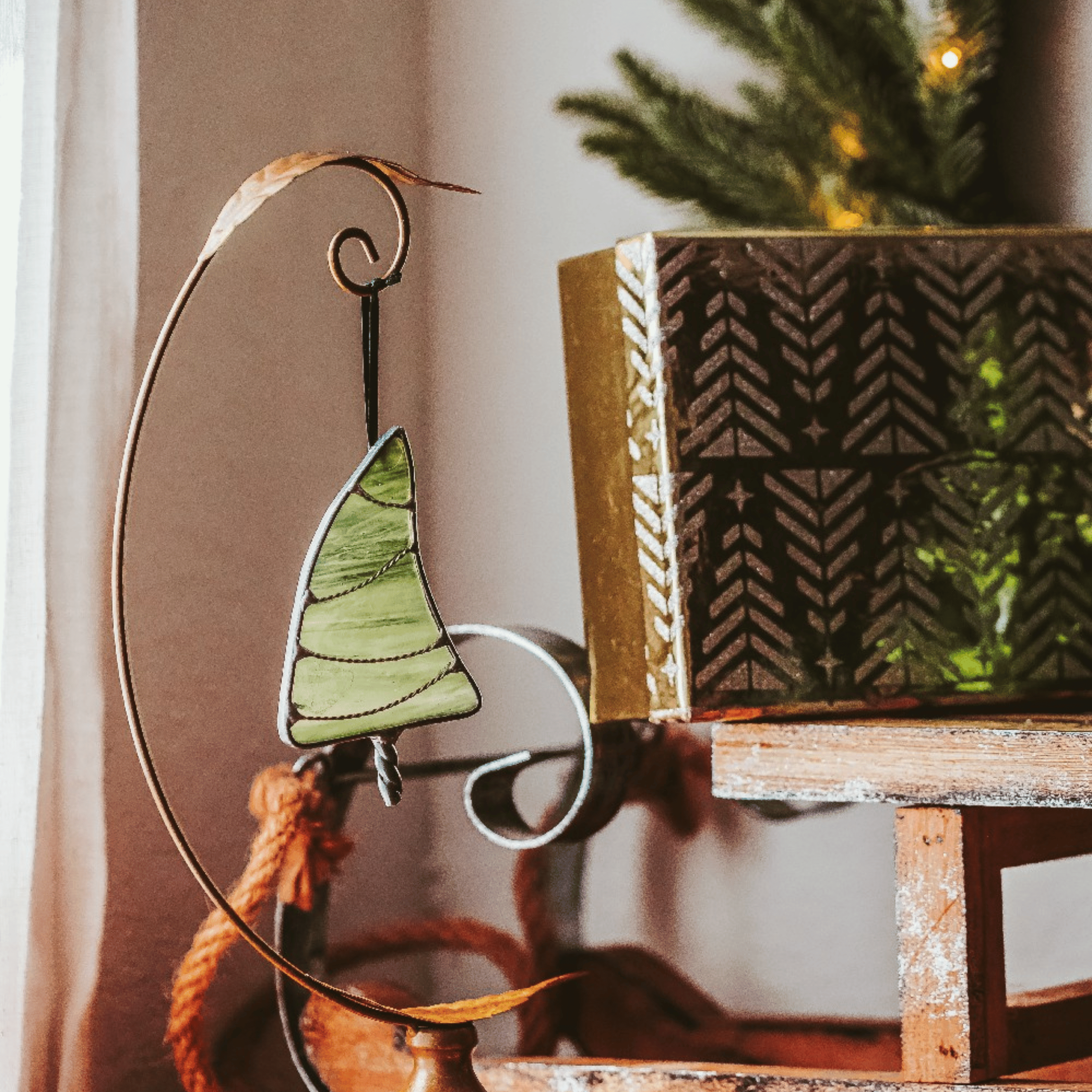 Classic green stained glass Christmas tree ornament with hand twisted metal garland and trunk on a holiday background, backlit