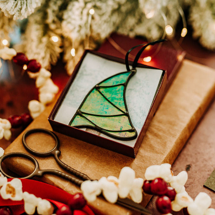 Iridescent green Whimsical Christmas Tree stained glass ornament with scissors and gift box on a festive background