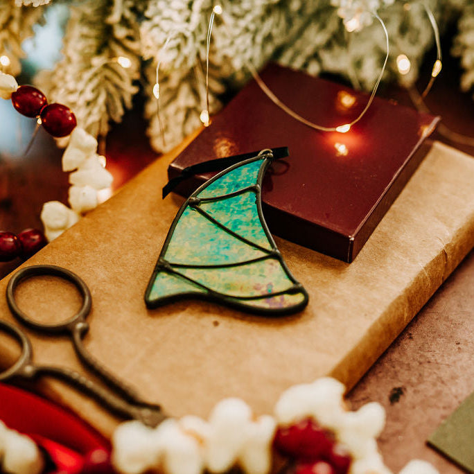 Decorative Christmas tree ornament on a piece of cardboard with scissors, surrounded by festive decorations.
