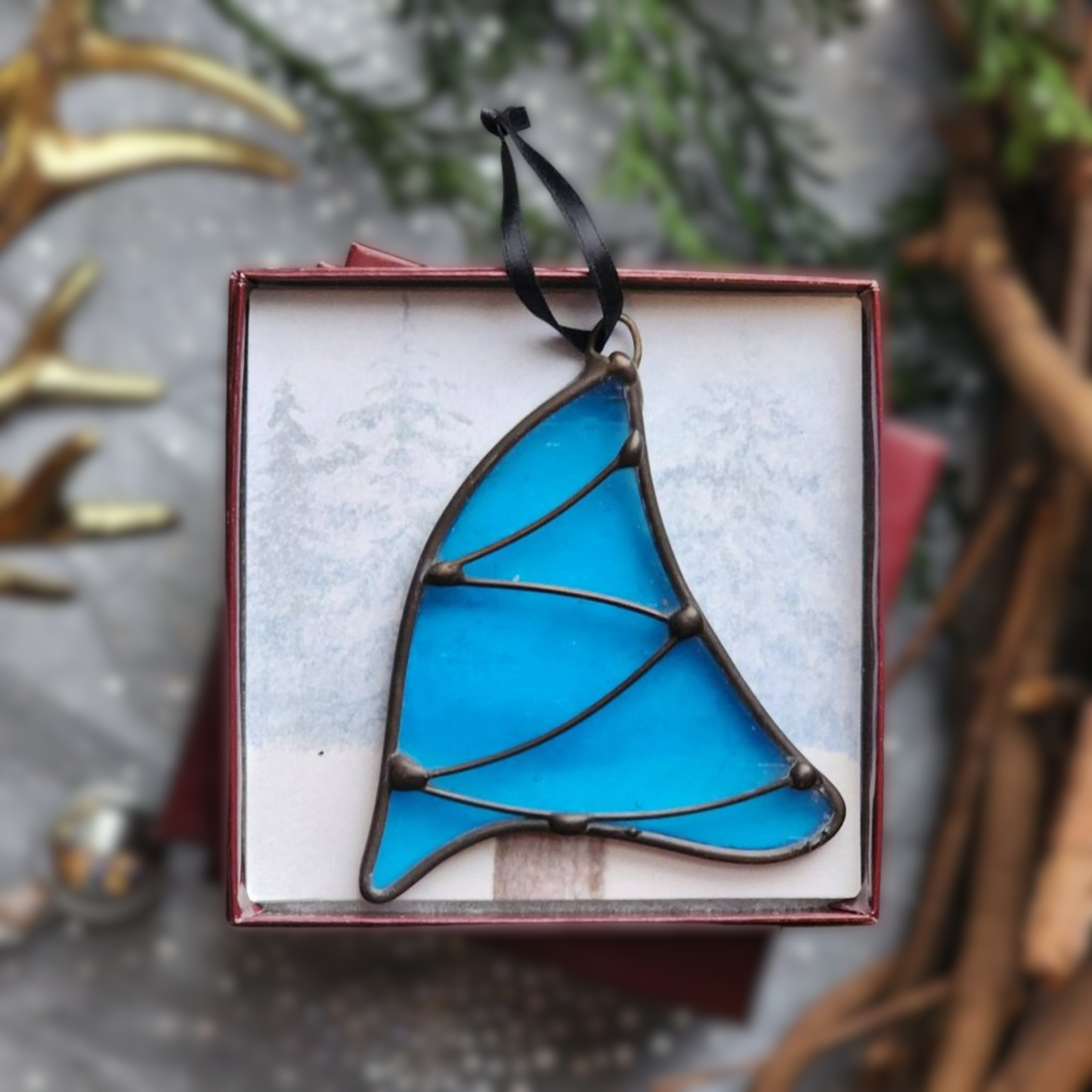 Topaz Blue Whimsical Christmas Tree stained glass ornament in a gift box on a festive background