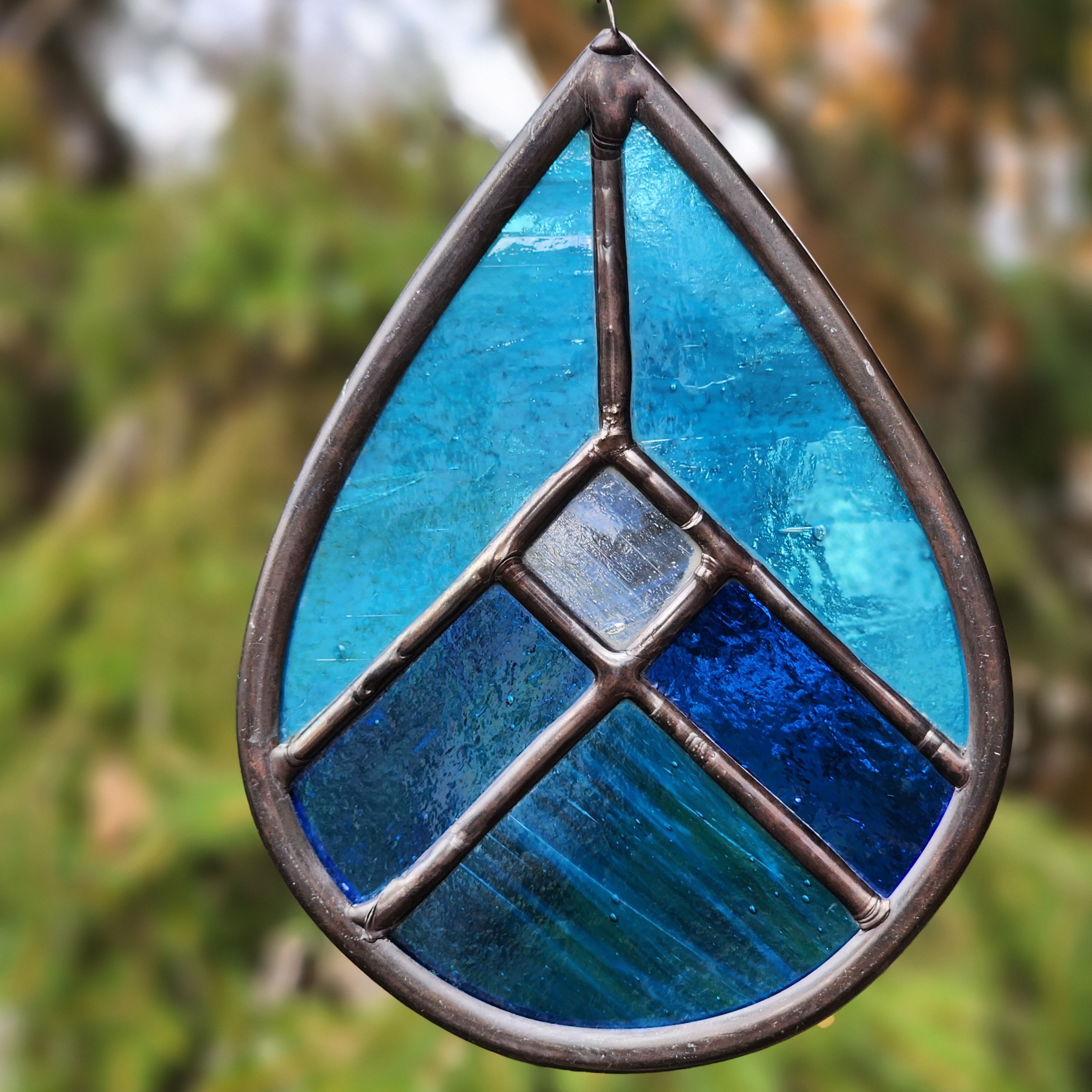 Blue geometric stained glass suncatcher on blurred outdoor background