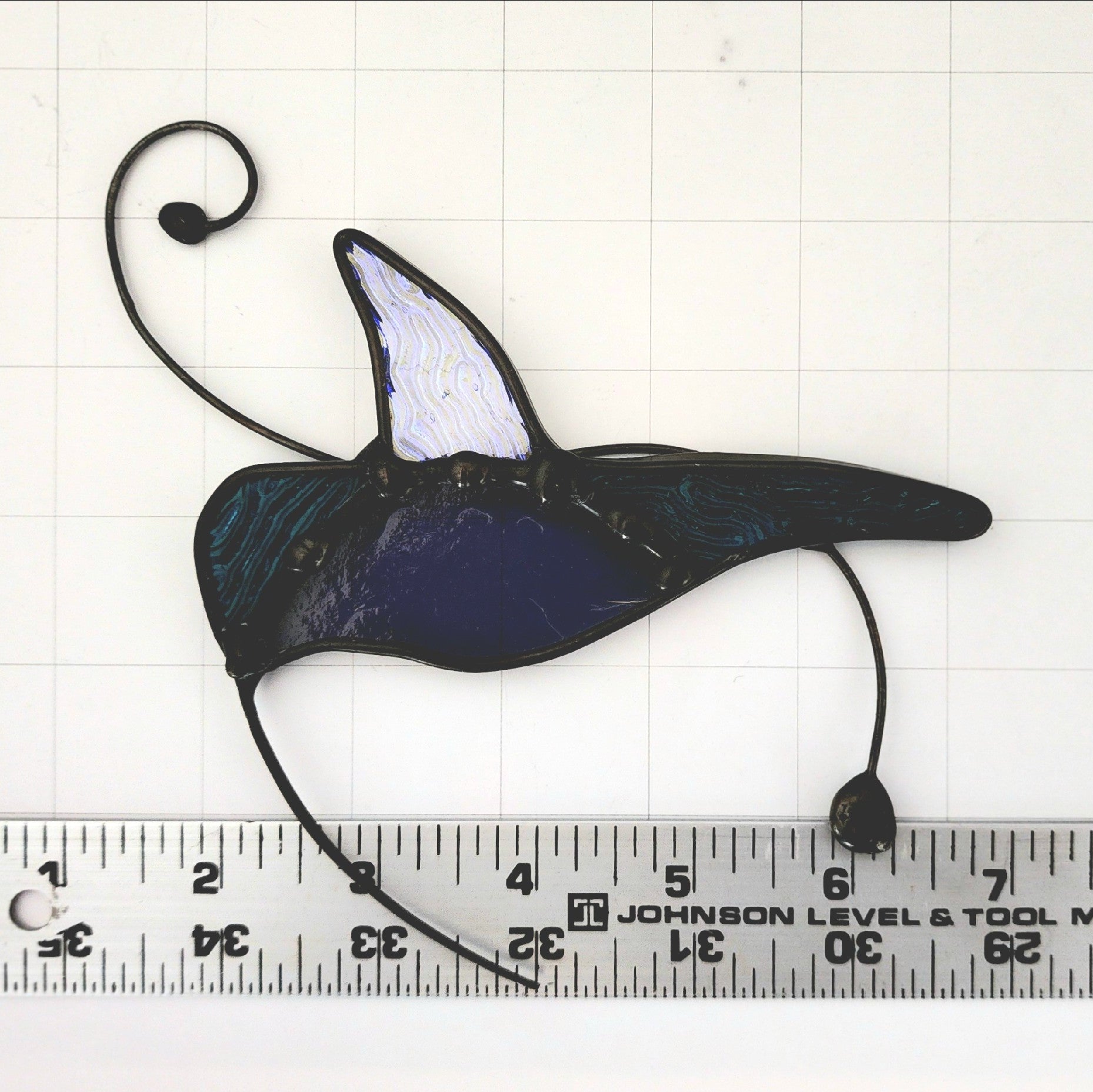 A stained glass hummingbird shown on a white grid background with a ruler along the bottom for scale. 